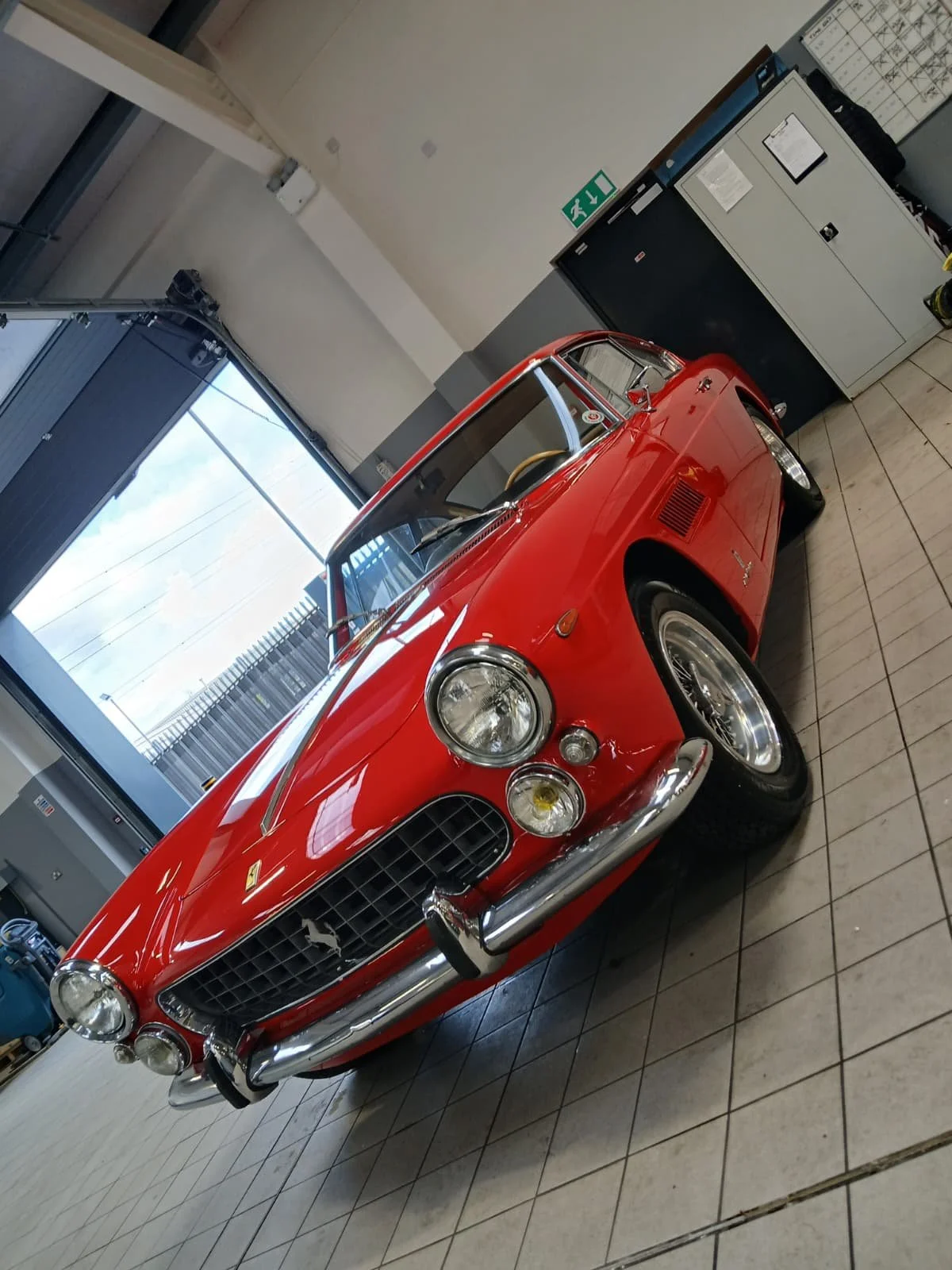A classic red sports car with a sleek design and chrome details is parked in a clean garage