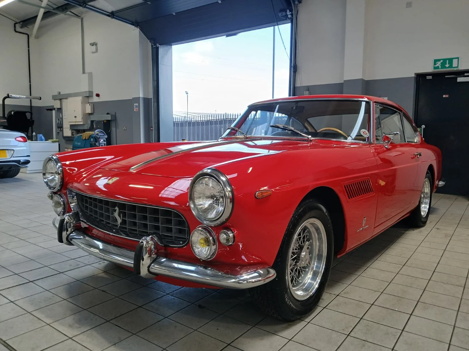 A classic red sports car with a sleek design and chrome details is parked in a clean garage