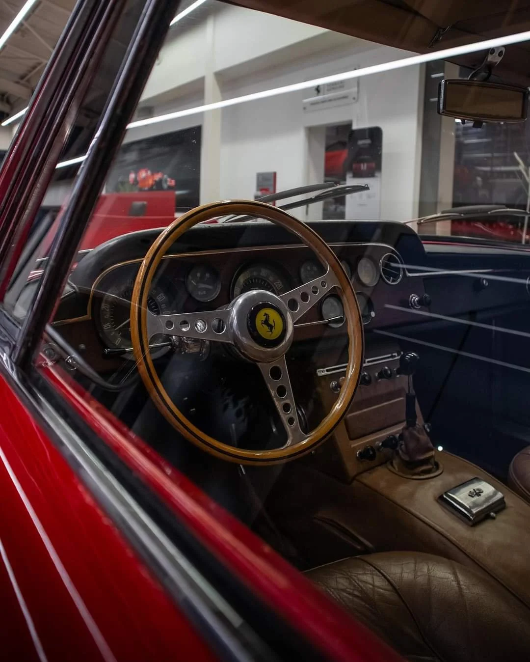 Interior view of a vintage car showcasing a wooden steering wheel with a yellow emblem, classic dashboard dials, and luxurious brown leather seats.