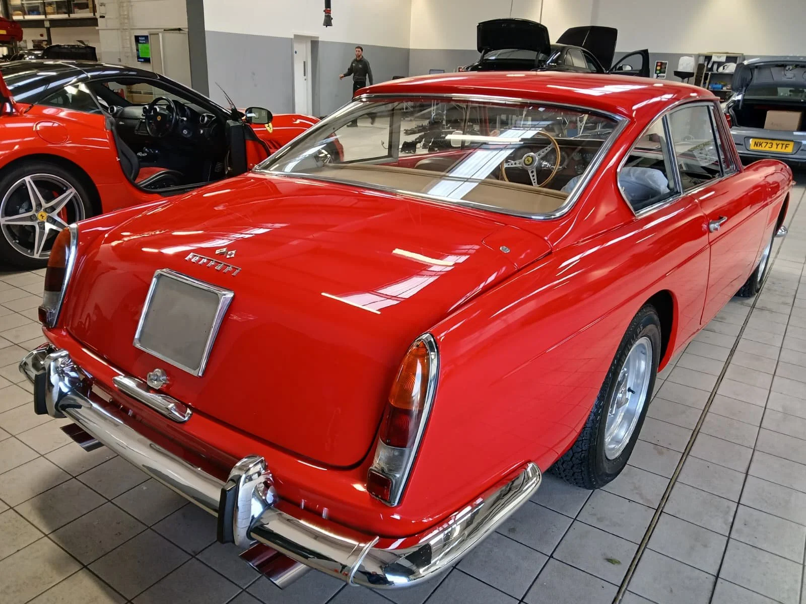 A classic red sports car with a sleek design and chrome details is parked in a clean garage