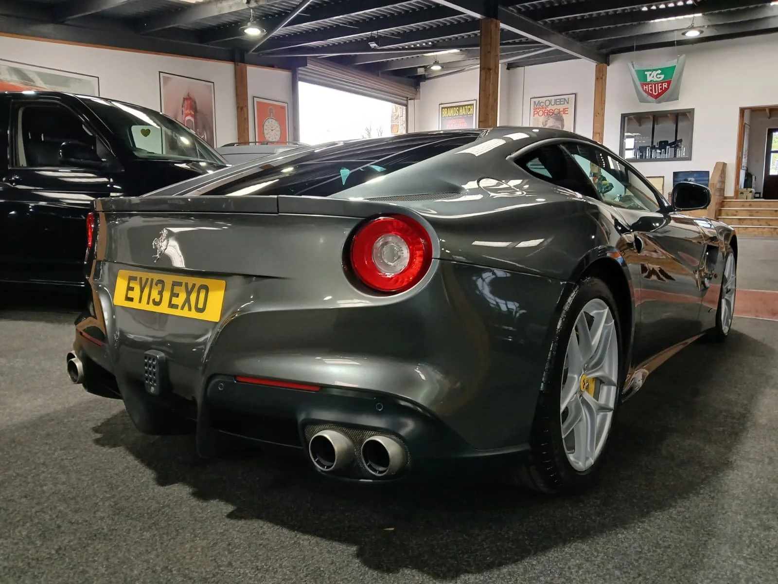 Gray sports car with sleek design inside a showroom. The rear features dual exhausts and distinct round taillights