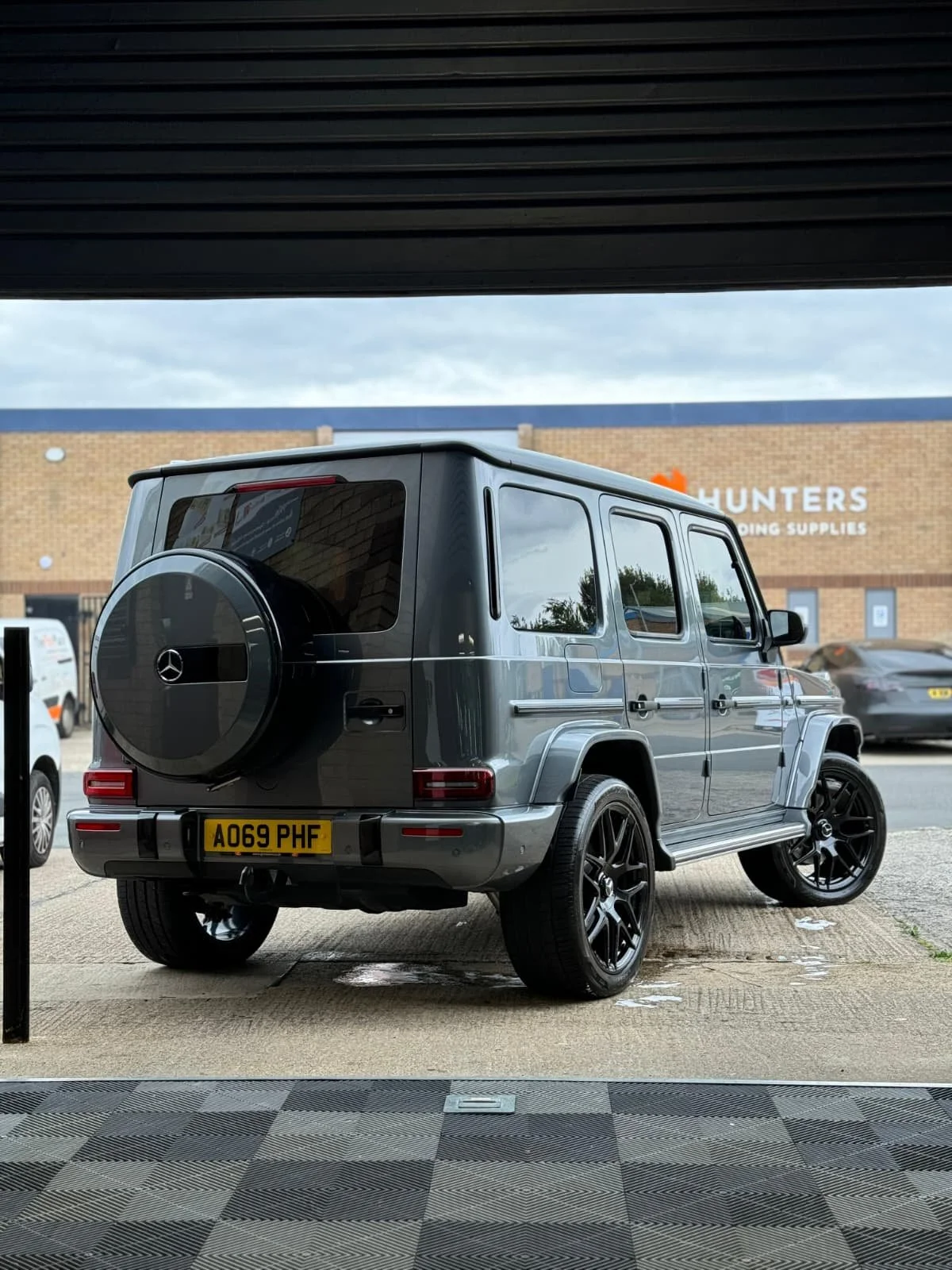 Dark gray Mercedes-Benz G-Class SUV parked on a checkered floor, with a visible rear tire cover