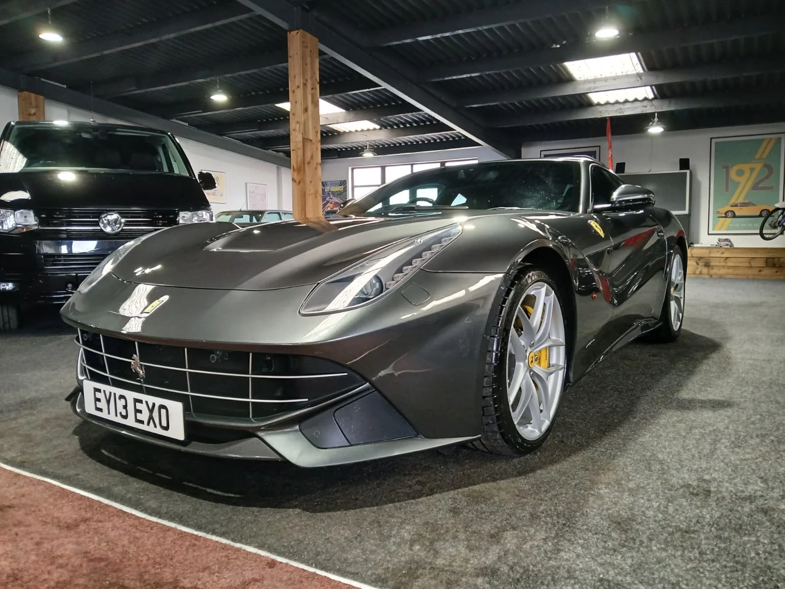 A sleek, grey sports car with a polished finish on display in a showroom. It features distinctive curves and a prominent front grille