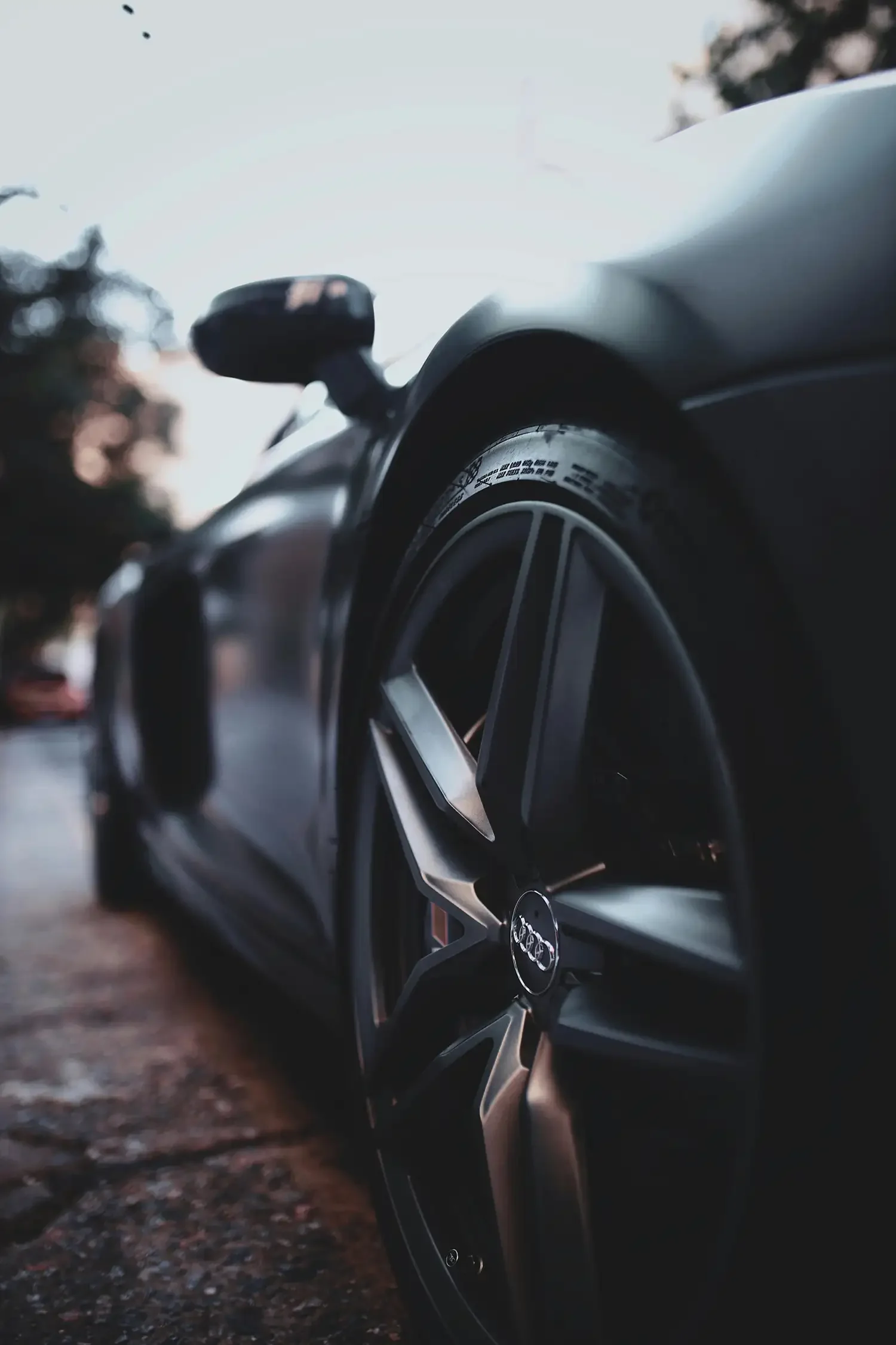 Close-up of a sleek black sports car wheel. The background is blurred, highlighting the vehicle's glossy finish and modern design.