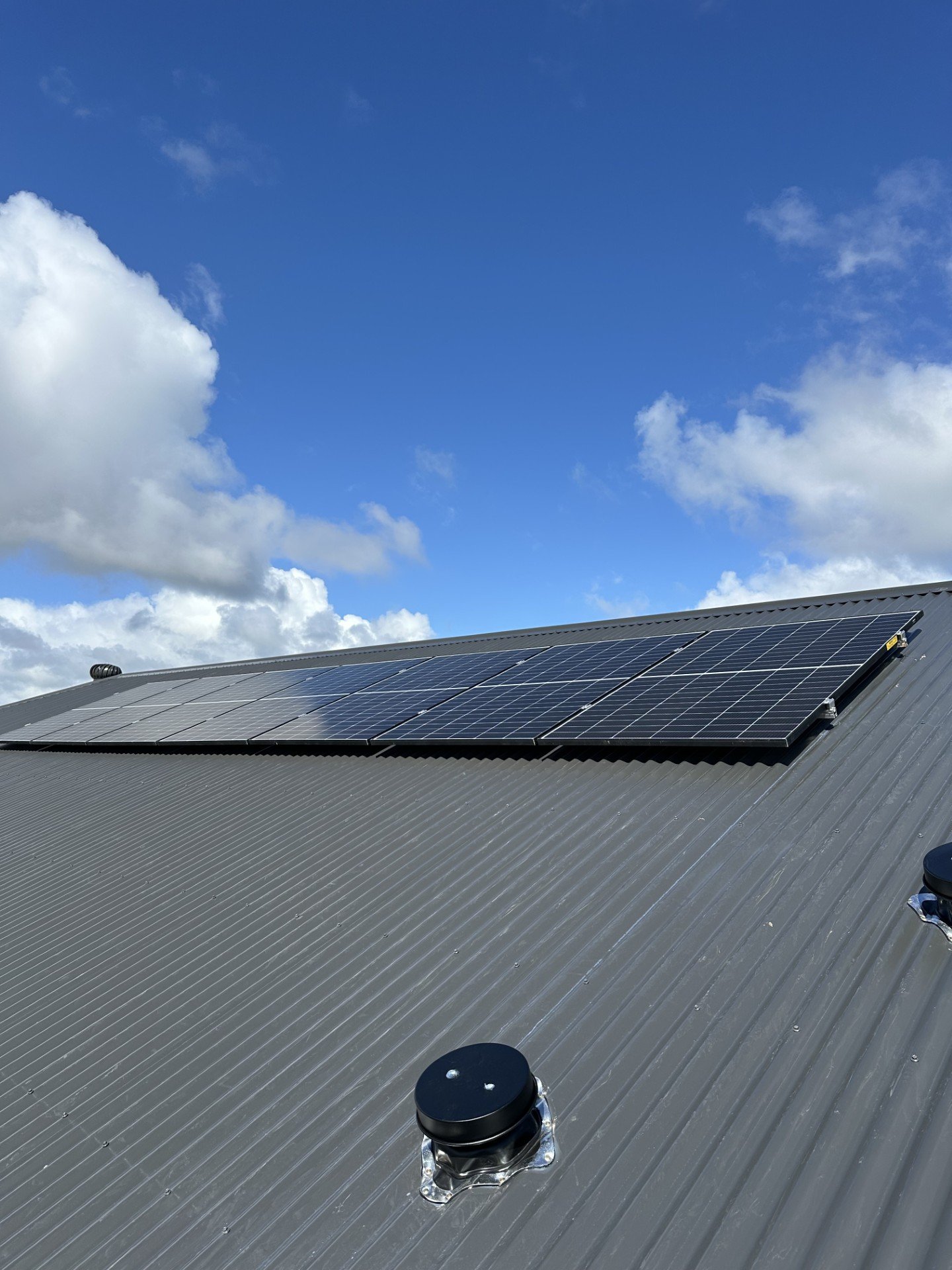 Solar panels installed on a metal rooftop against a bright blue sky with scattered clouds.