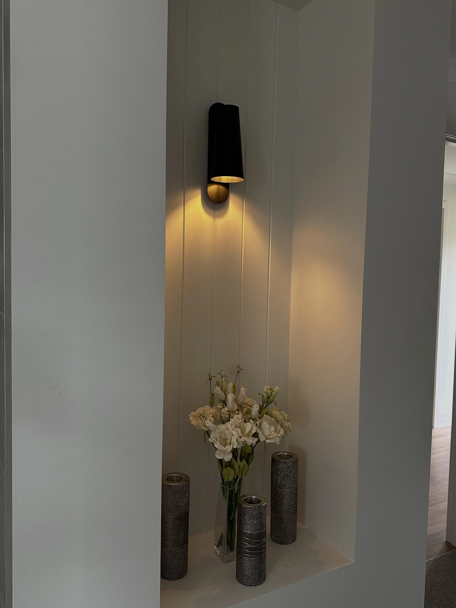 Wall sconce light with a vase of white roses and three candles in a built-in wall niche.