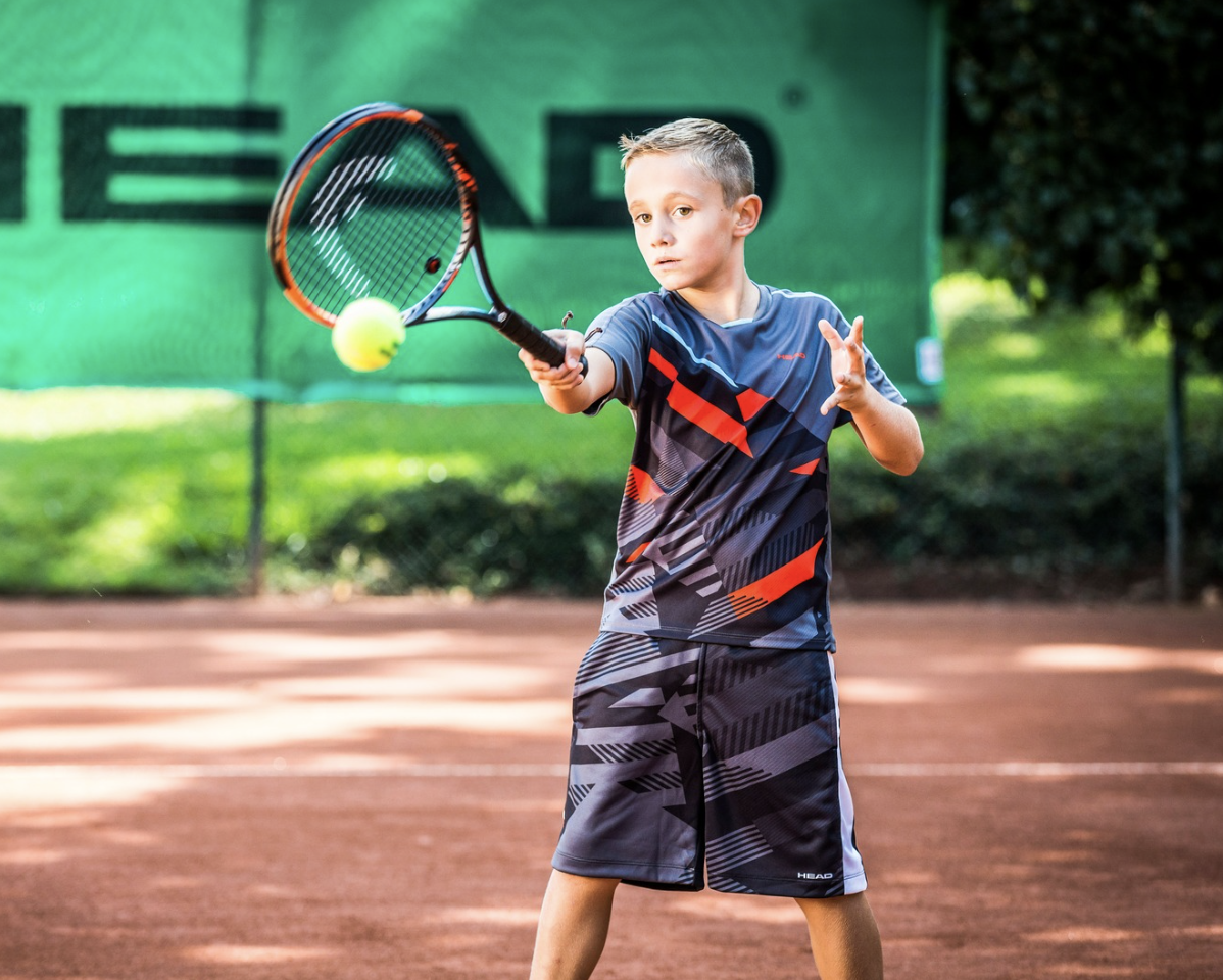 A young boy on a tennis court hitting a tennis ball with a racket.