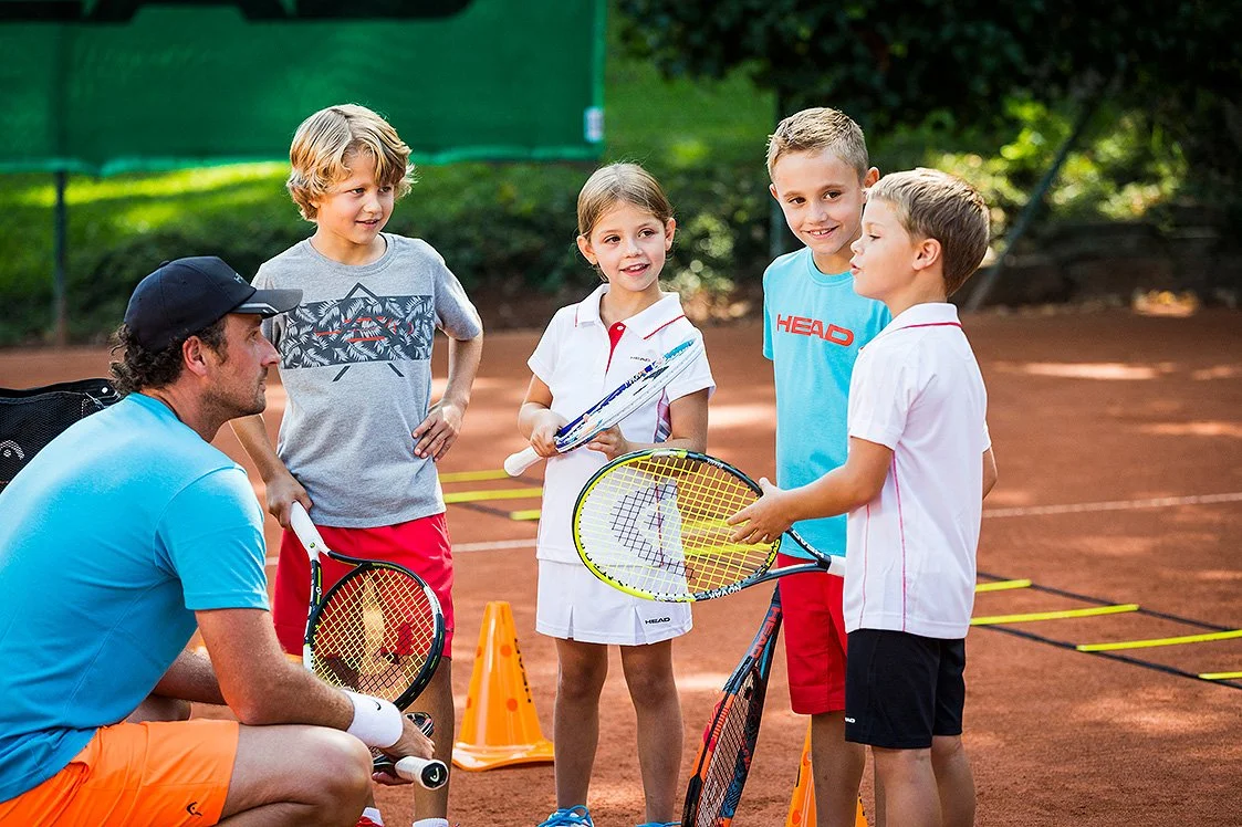 Tennis coach instructing four children on a clay tennis court