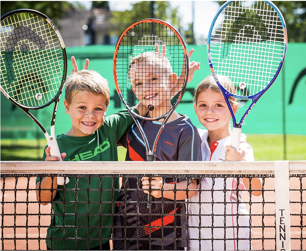 Three children holding tennis rackets on a tennis court.