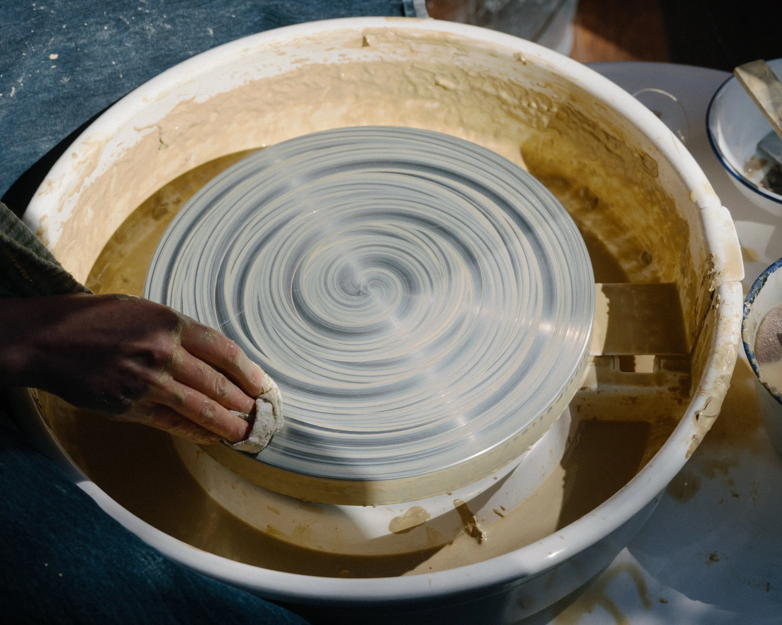 A person is polishing a ceramic plate on a rotating wheel in a pottery studio.