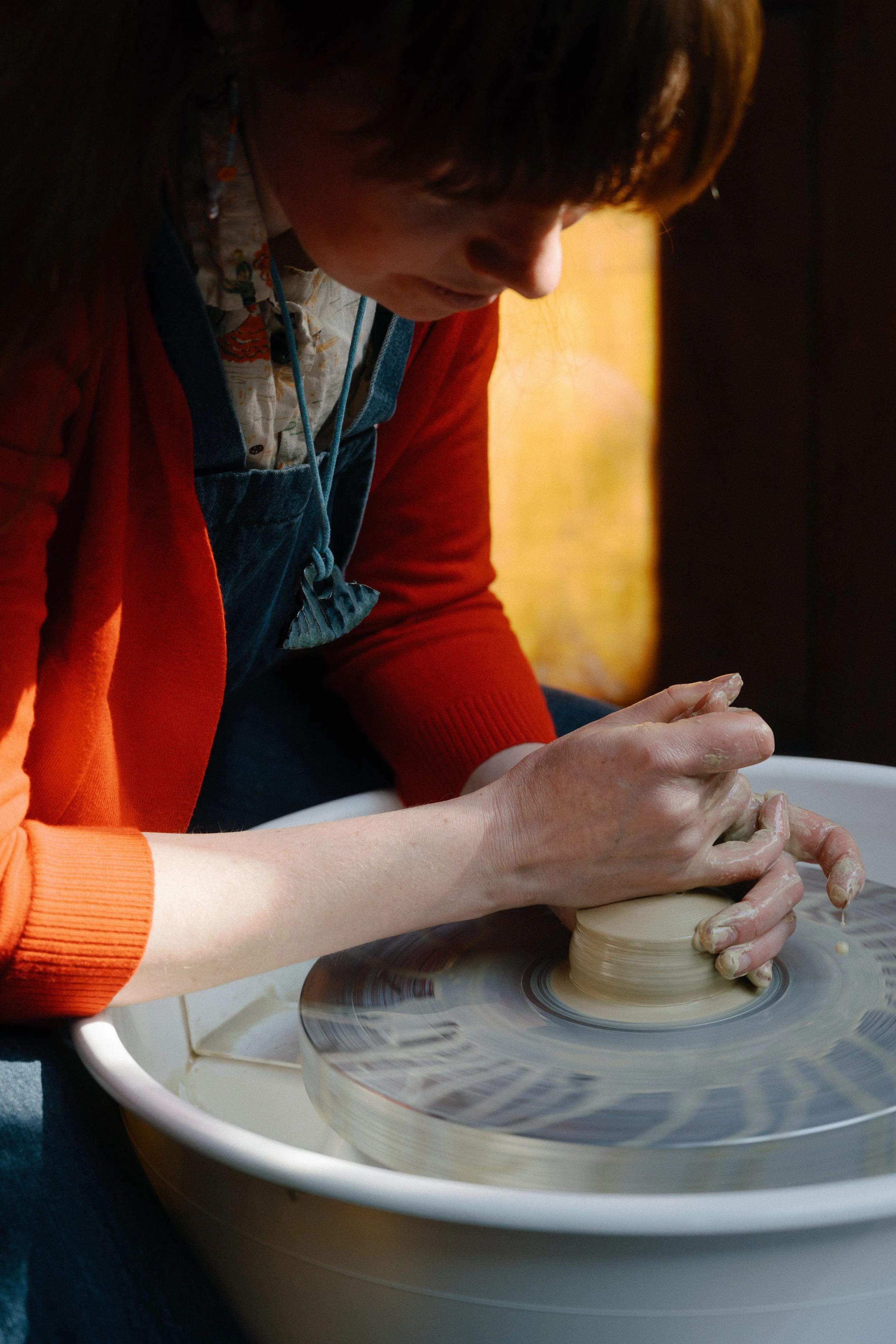A person shaping clay on a pottery wheel with their hands.