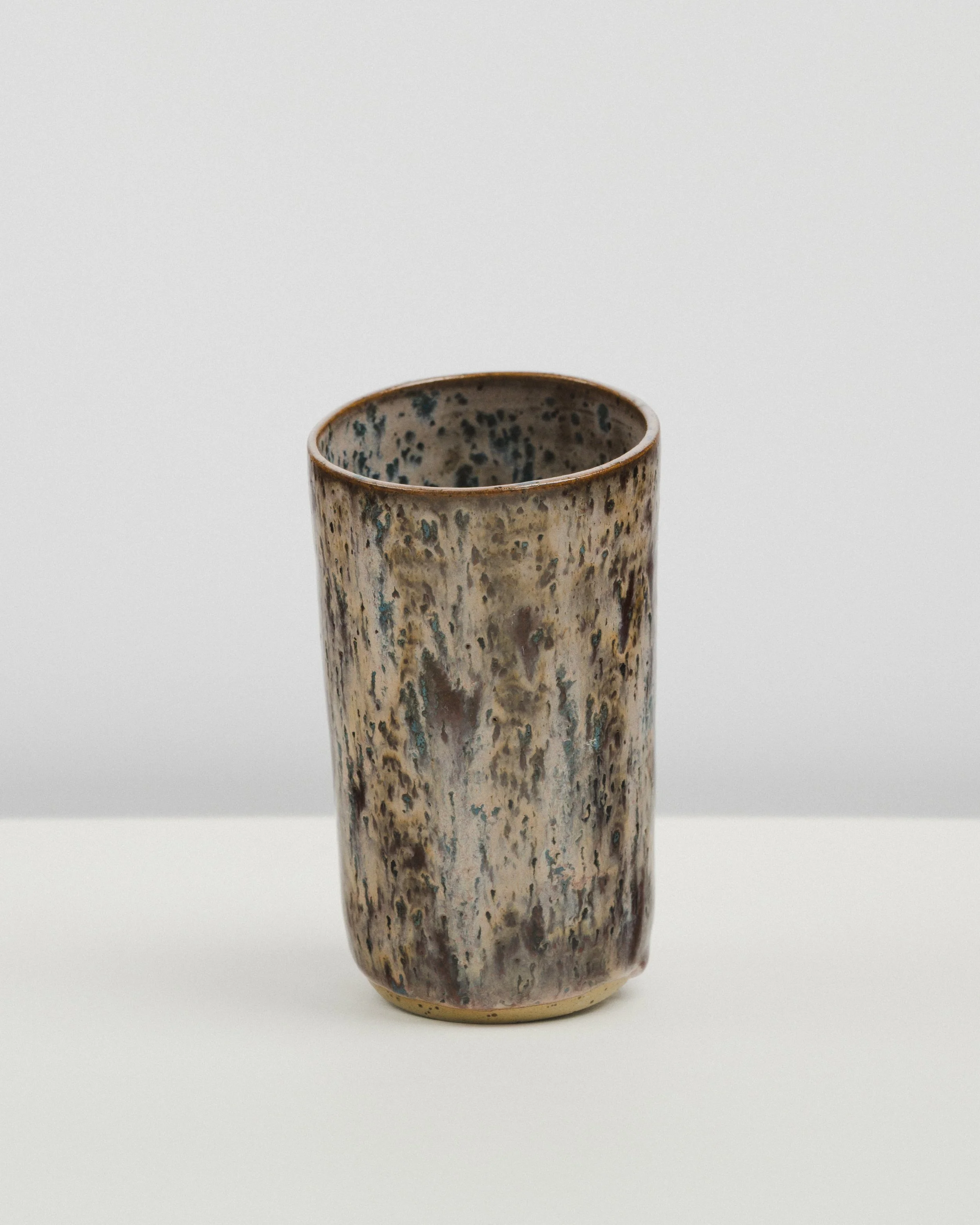 Ceramic vase with a speckled, textured glaze, standing on a plain white surface against a white background.