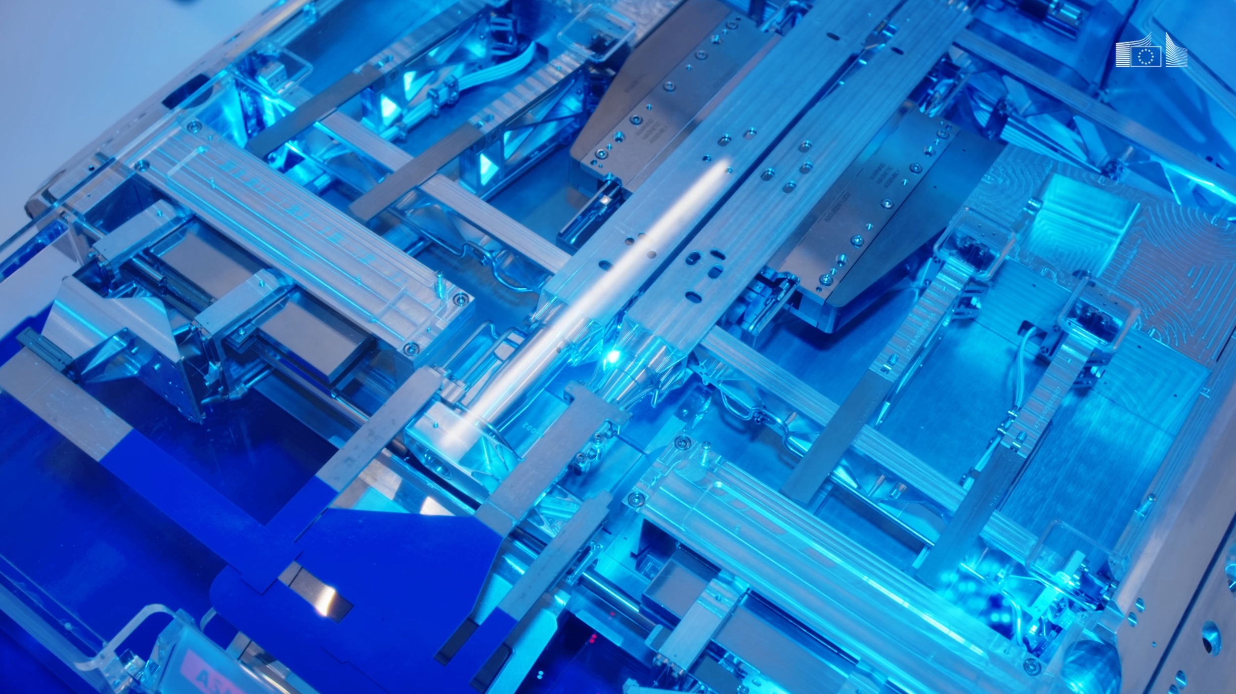 Close-up of a futuristic, transparent, blue-lit scientific or technological equipment with intricate metallic components and circuitry.