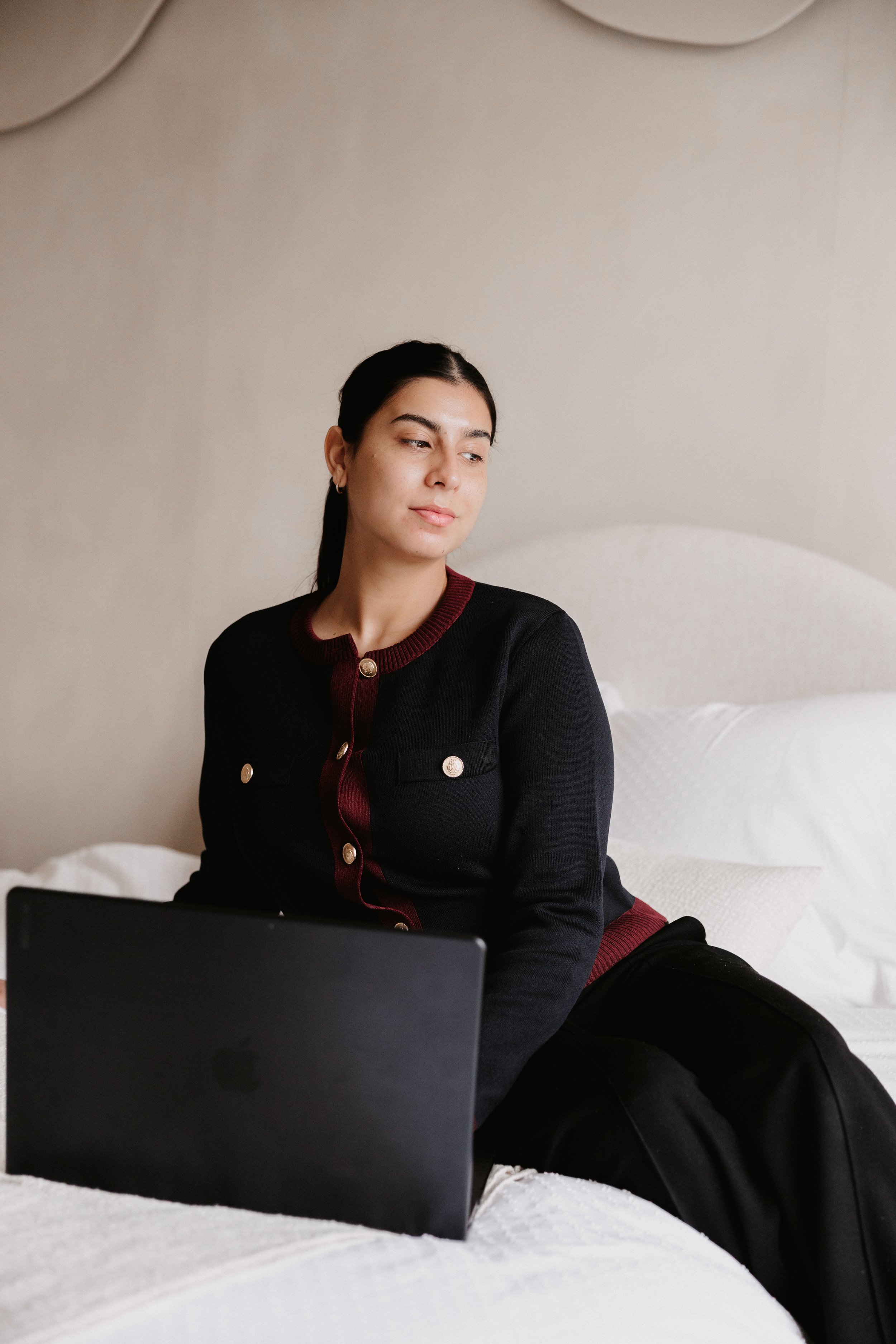 Vrouw zit op een bed met een open laptop voor zich, in een rustige, lichte kamer.
