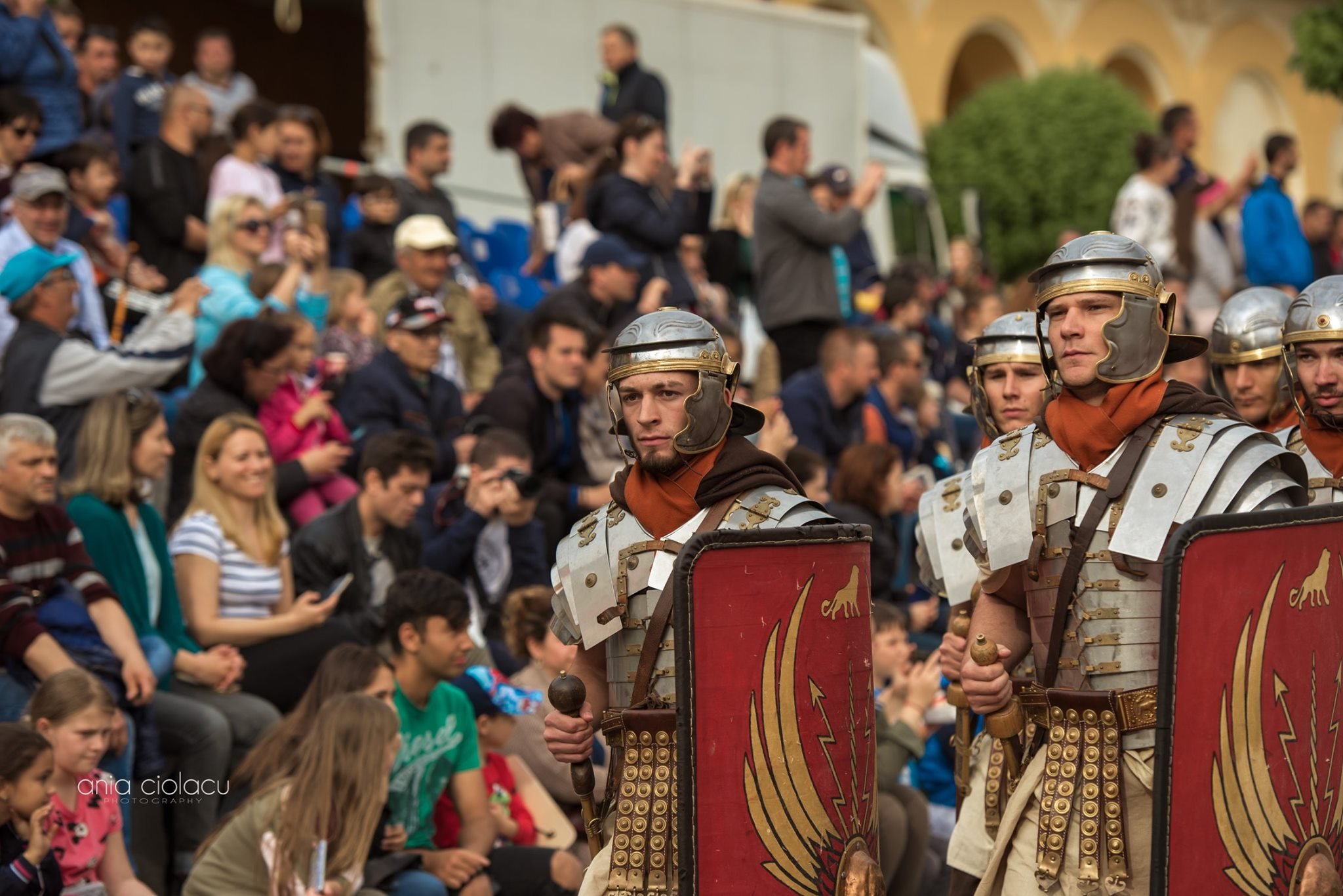 Roman soldiers in armor participating in a historical reenactment parade, with a crowd of spectators watching.