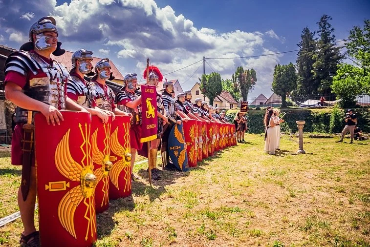 People dressed as Roman soldiers with shields and armor standing in a line outdoors during daytime.