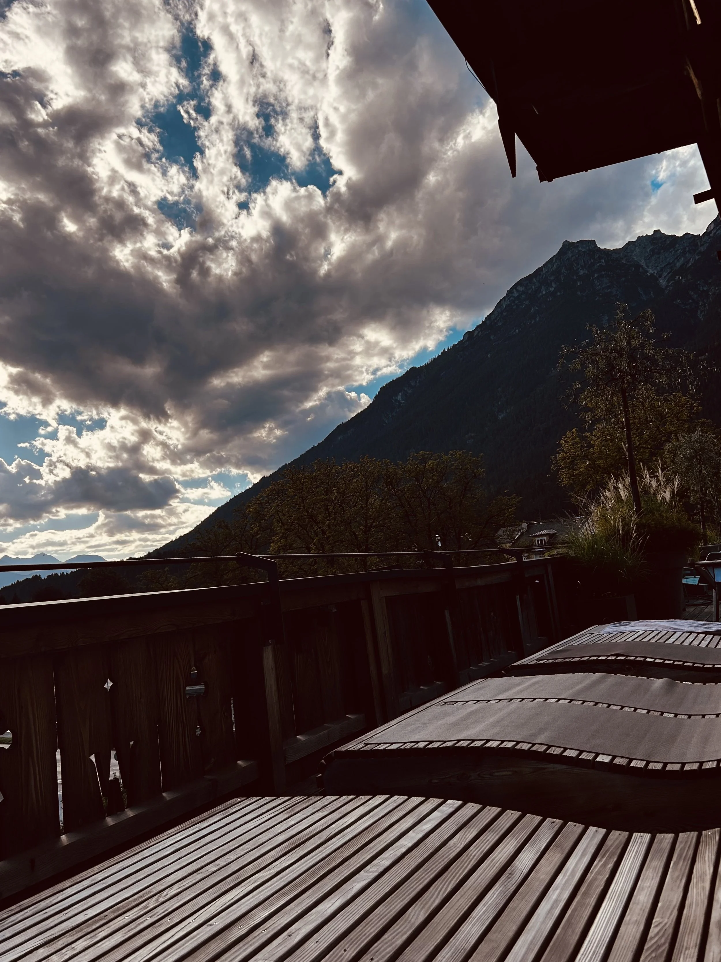 Blick von einem Balkon mit Holzterrasse auf Berge und bewölkten Himmel.