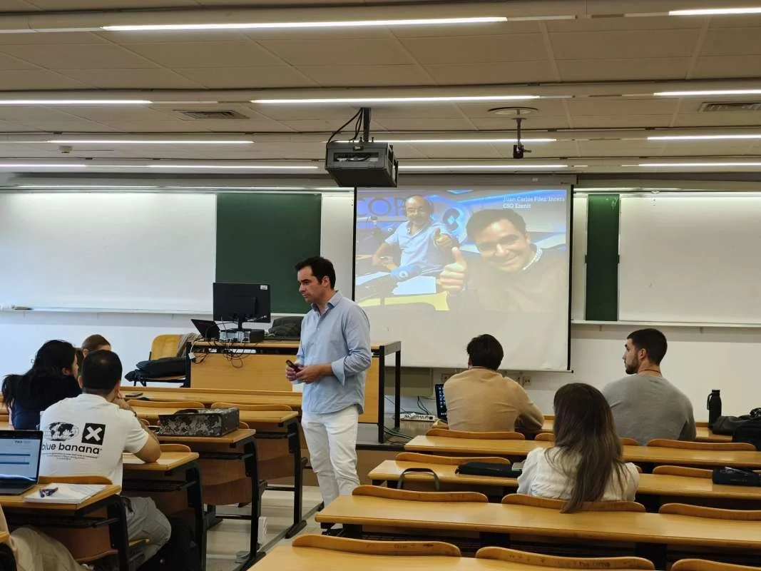Clase en un aula universitaria con estudiantes y un profesor frente a un pizarrón y proyector