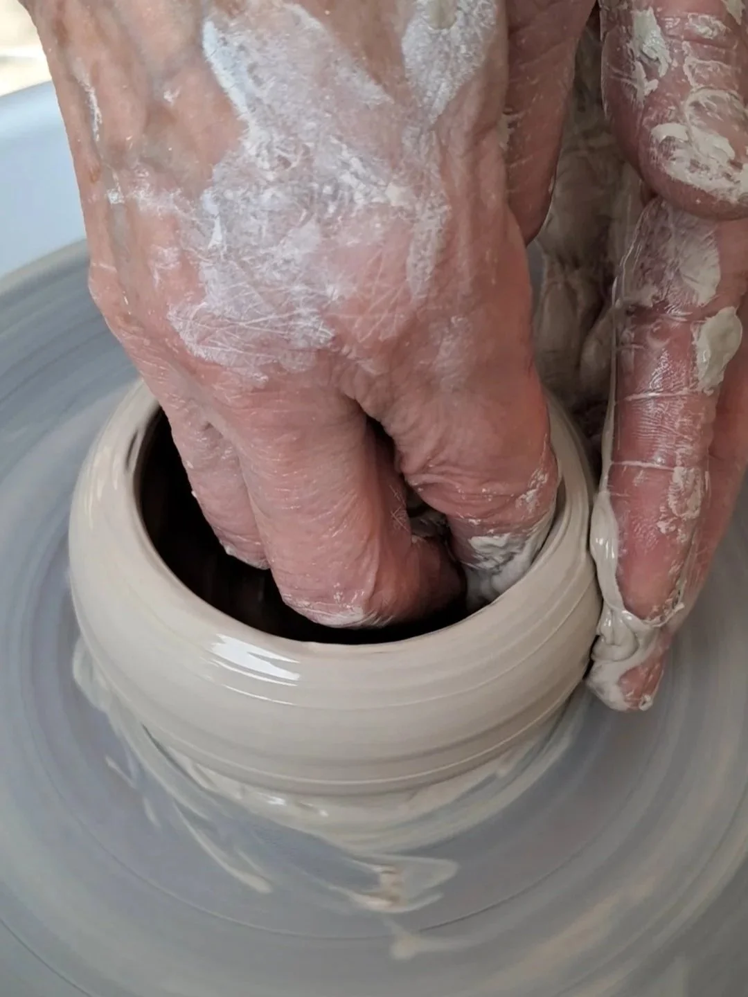 Une main d'adulte façonnant de la poterie en argile sur un tour de potier.