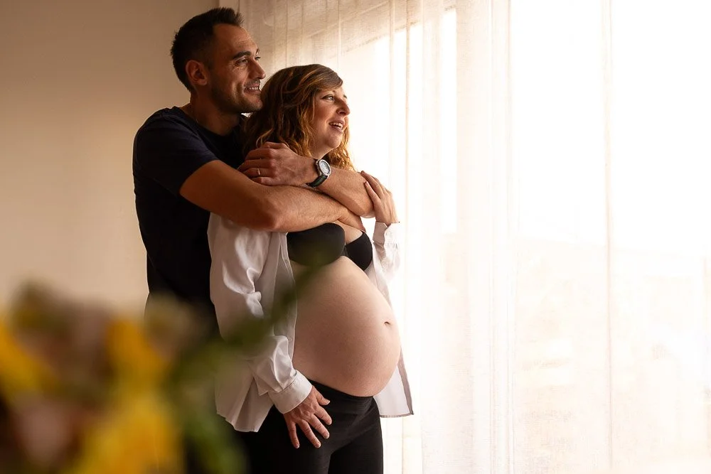 Un couple heureux, un homme et une femme enceinte, se tenant près d'une fenêtre ensoleillée. Reportage photo bébé côte d’opale, Dunkerque, Calais, Wissant, Wimereux, Boulogne-sur-Mer, Hardelot-plage, Le Touquet, Lille, sangatte.