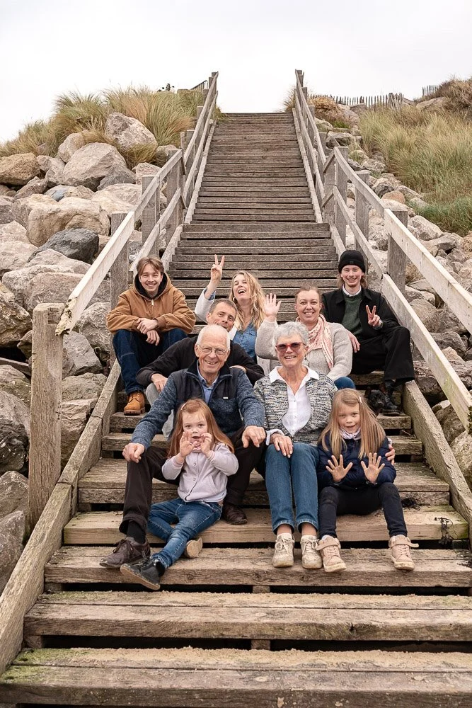 Groupe de neuf personnes, un couple âgé, des adultes et des enfants, posant sur un escalier en bois à l'extérieur avec des rochers et de l'herbe autour.