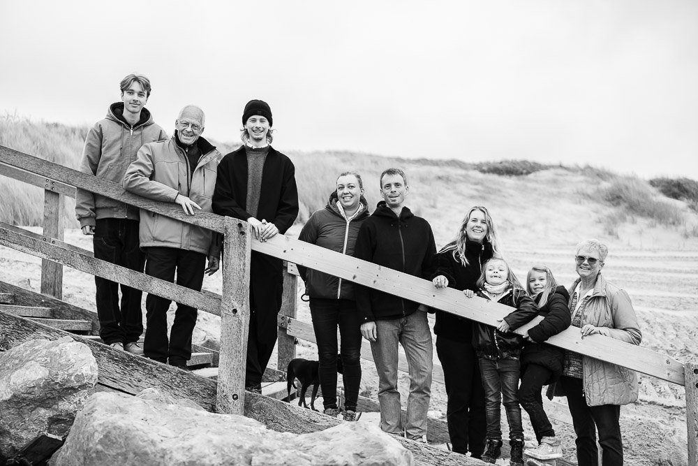 Famille souriante posant sur une rampe en bois à la plage, en groupe avec enfants et adultes, arrière-plan de dunes de sable. Reportage photo bébé côte d’opale, Dunkerque, Calais, Wissant, Wimereux, Boulogne-sur-Mer, Hardelot-plage, Le Touquet, Lille