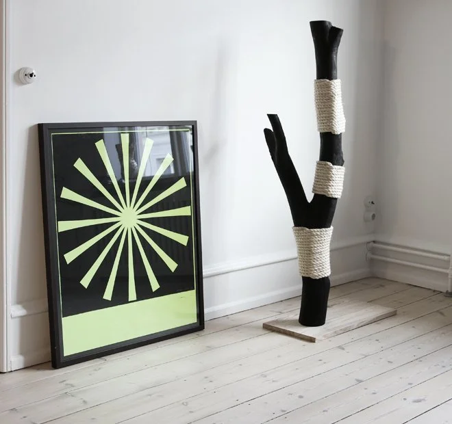 Sculptural wooden cat scratching post with white rope, placed beside framed artwork