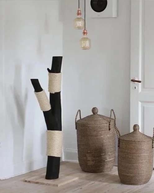 Black wooden cat scratching post with beige rope, placed in a minimalist interior with woven baskets
