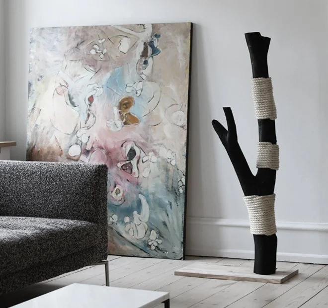 Sculptural black cat scratching post with white rope, positioned beside a sofa and artwork