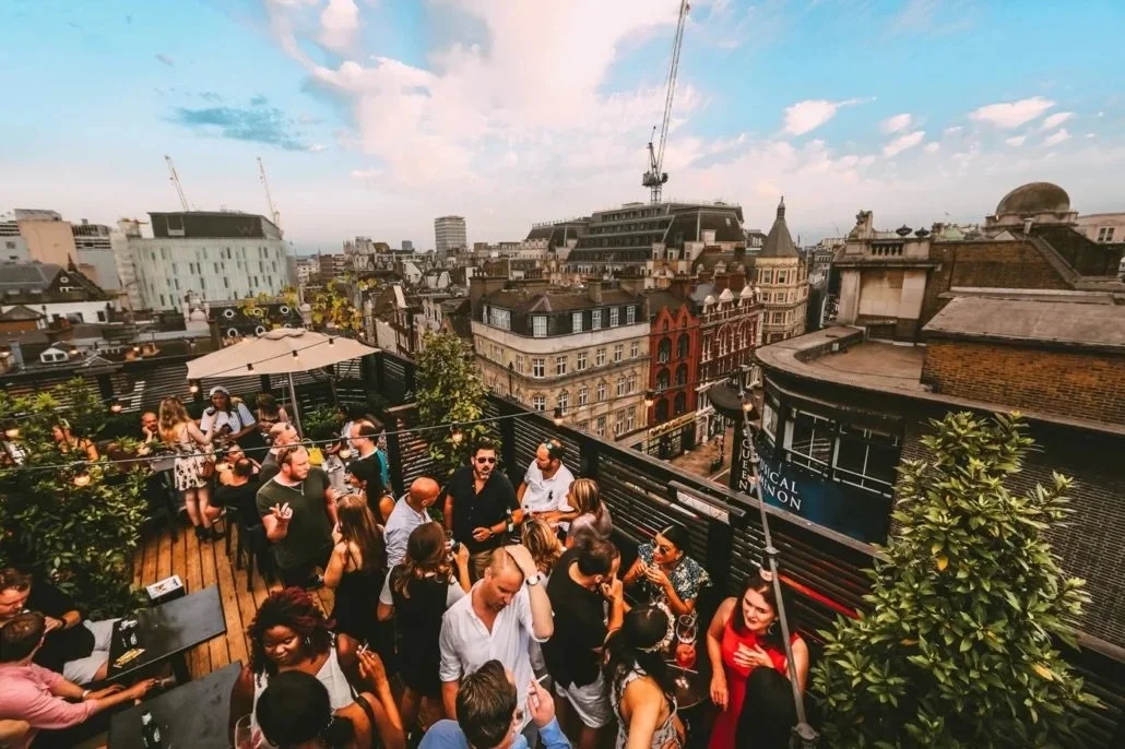 People socializing on a rooftop terrace with city buildings in the background.