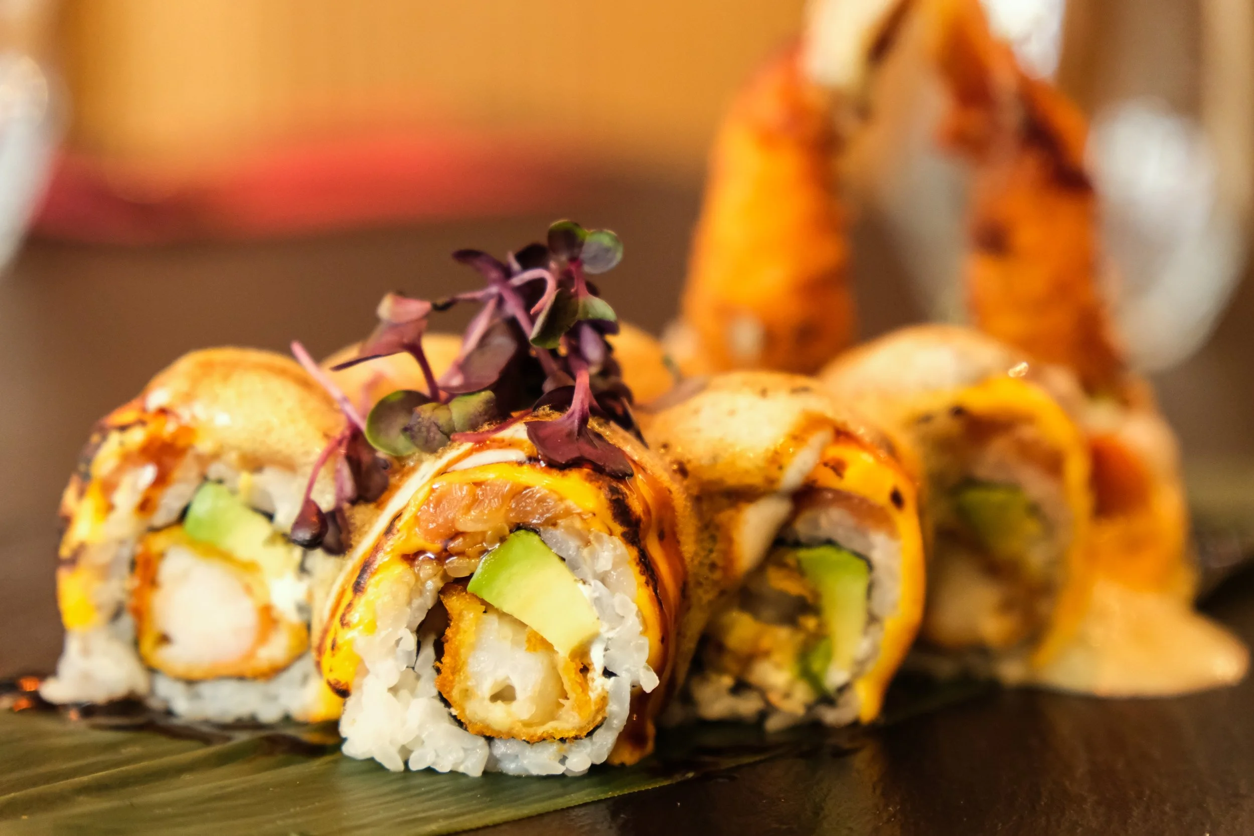 Close-up of sushi rolls garnished with microgreens, on a dark plate