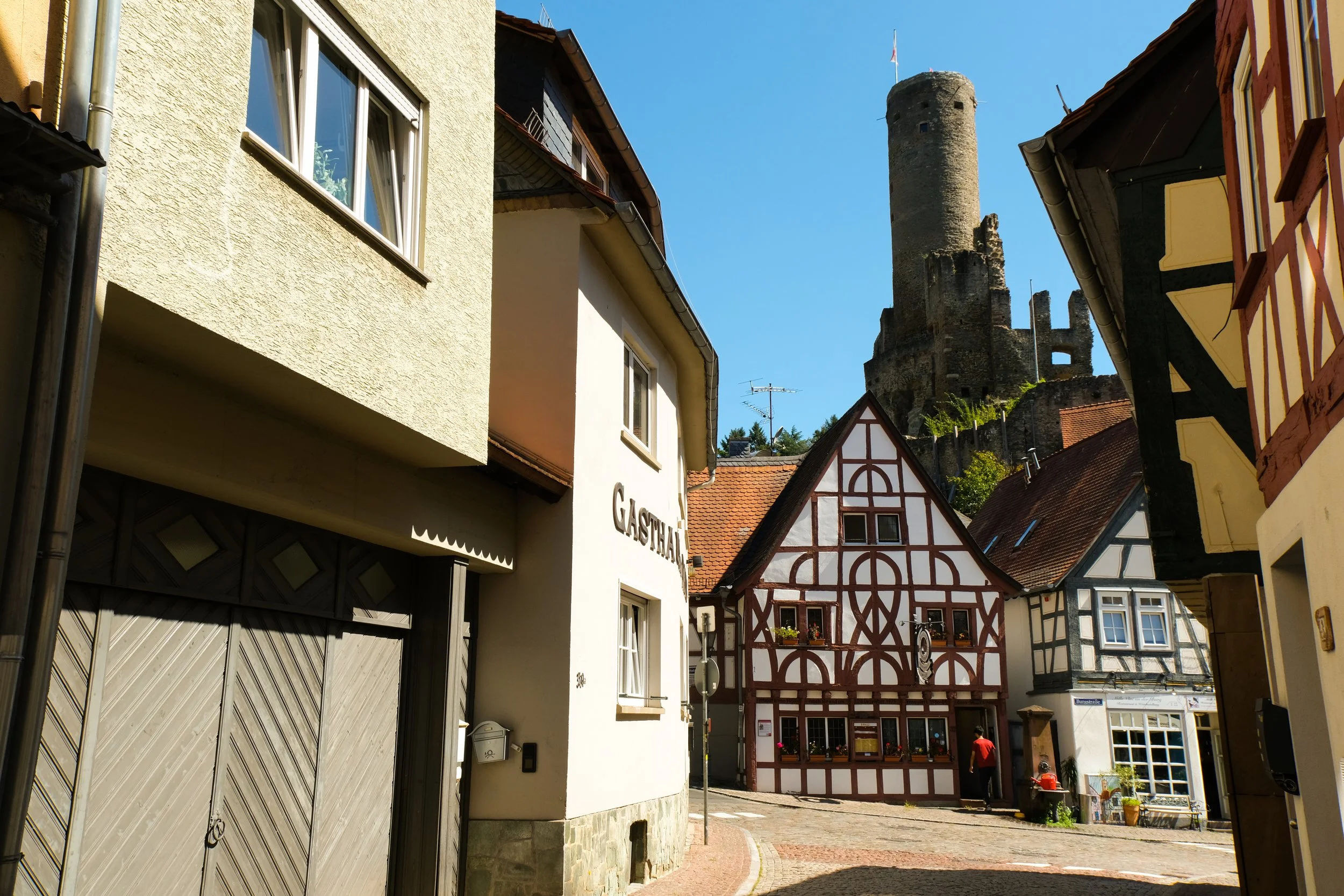 A street scene in a European town with colorful, traditional half-timbered houses and a castle in the background.