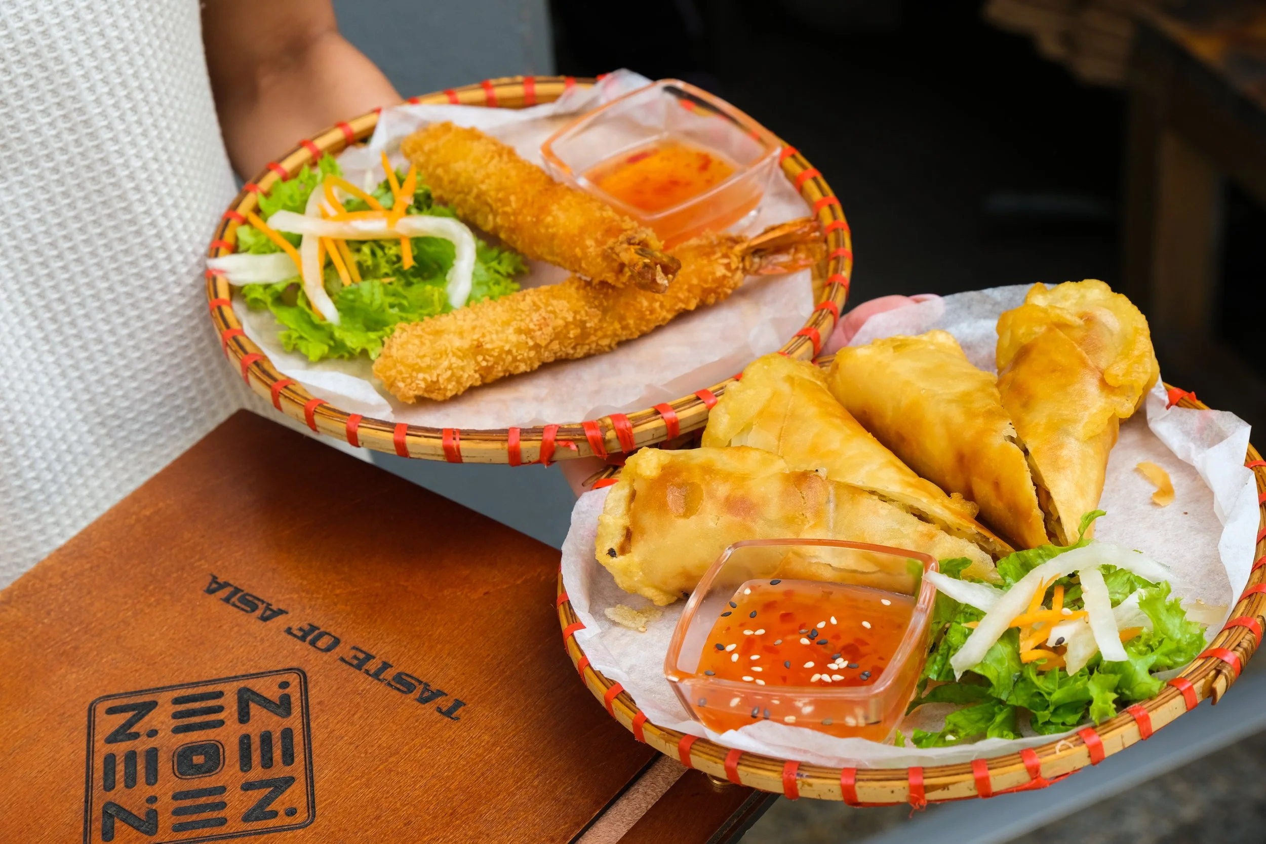 Two baskets of Vietnamese spring rolls, fried egg rolls, and fried shrimp with dipping sauces, lettuce, and shredded carrots.