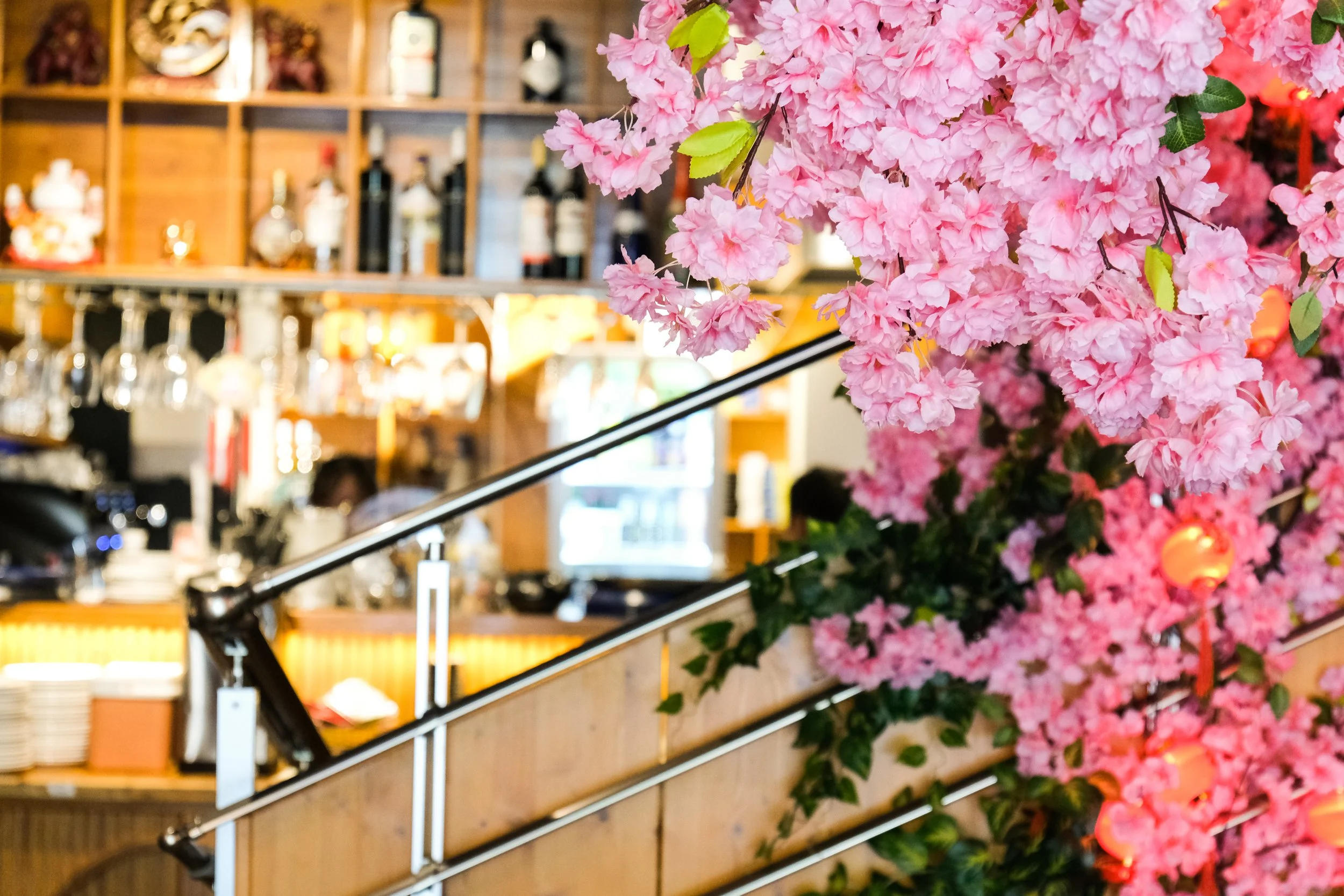 Pink cherry blossom flowers near a bar with bottles and glassware, blurred background.