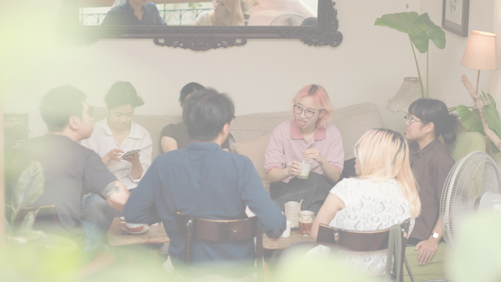Group of seven young adults socializing in a cozy cafe, sitting around a wooden table with drinks and snacks, engaging in conversation.