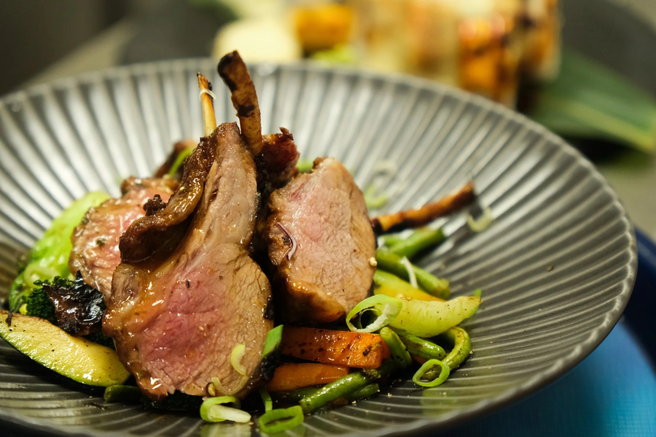 Close-up of cooked lamb chops with vegetables on a gray plate.