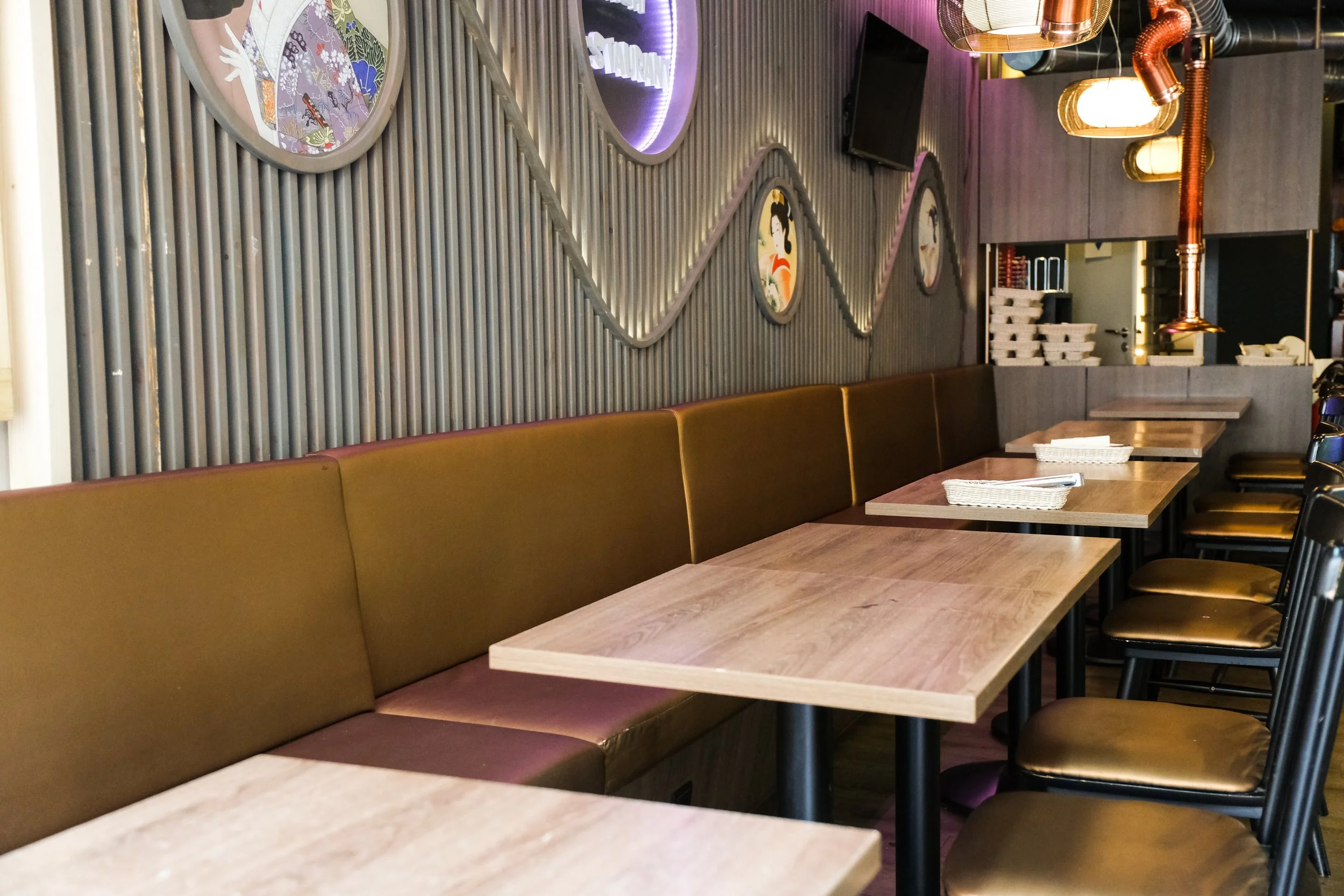 Empty restaurant with wooden tables, brown seats, and wall decorations including circular art and a television.