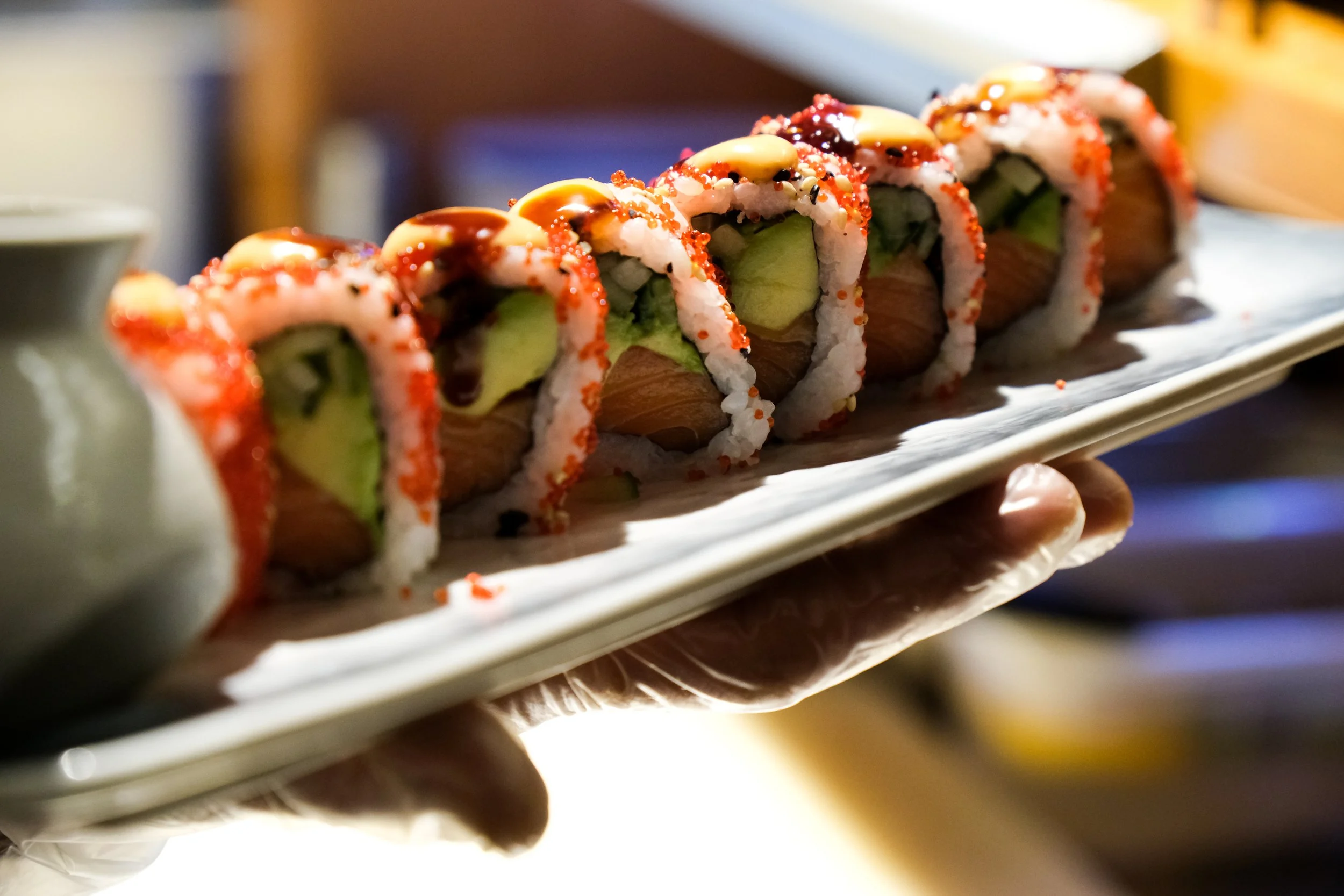 Sushi roll with rice, avocado, salmon, and toppings like eel sauce, drizzled with mayonnaise and garnished with red fish roe.