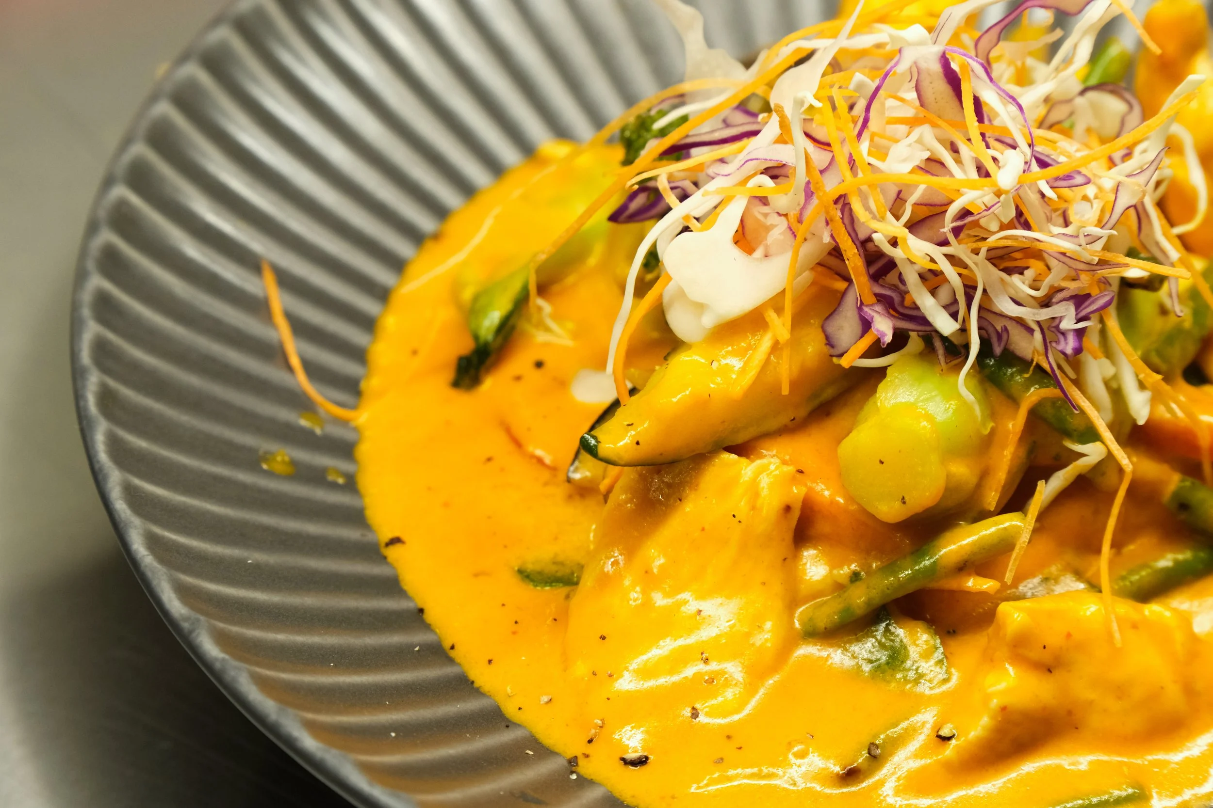 A dish of curry with vegetables and a side of shredded cabbage and carrots on a dark, textured plate.