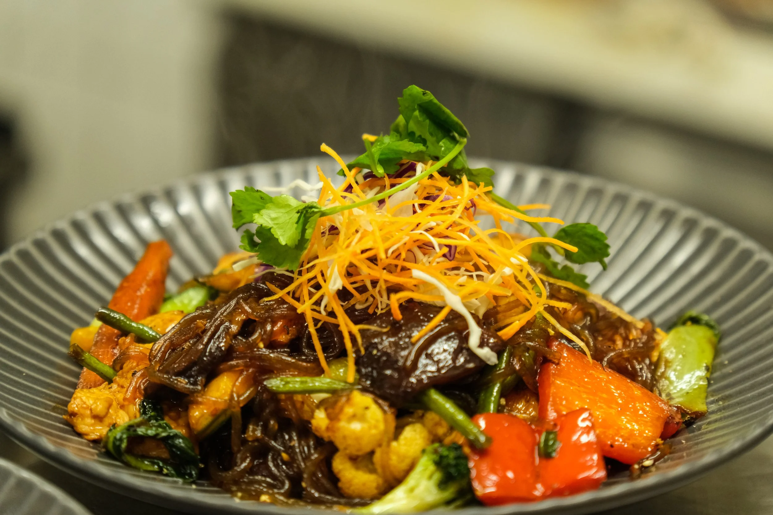 A bowl of stir-fried vegetables topped with shredded cheese and fresh cilantro.