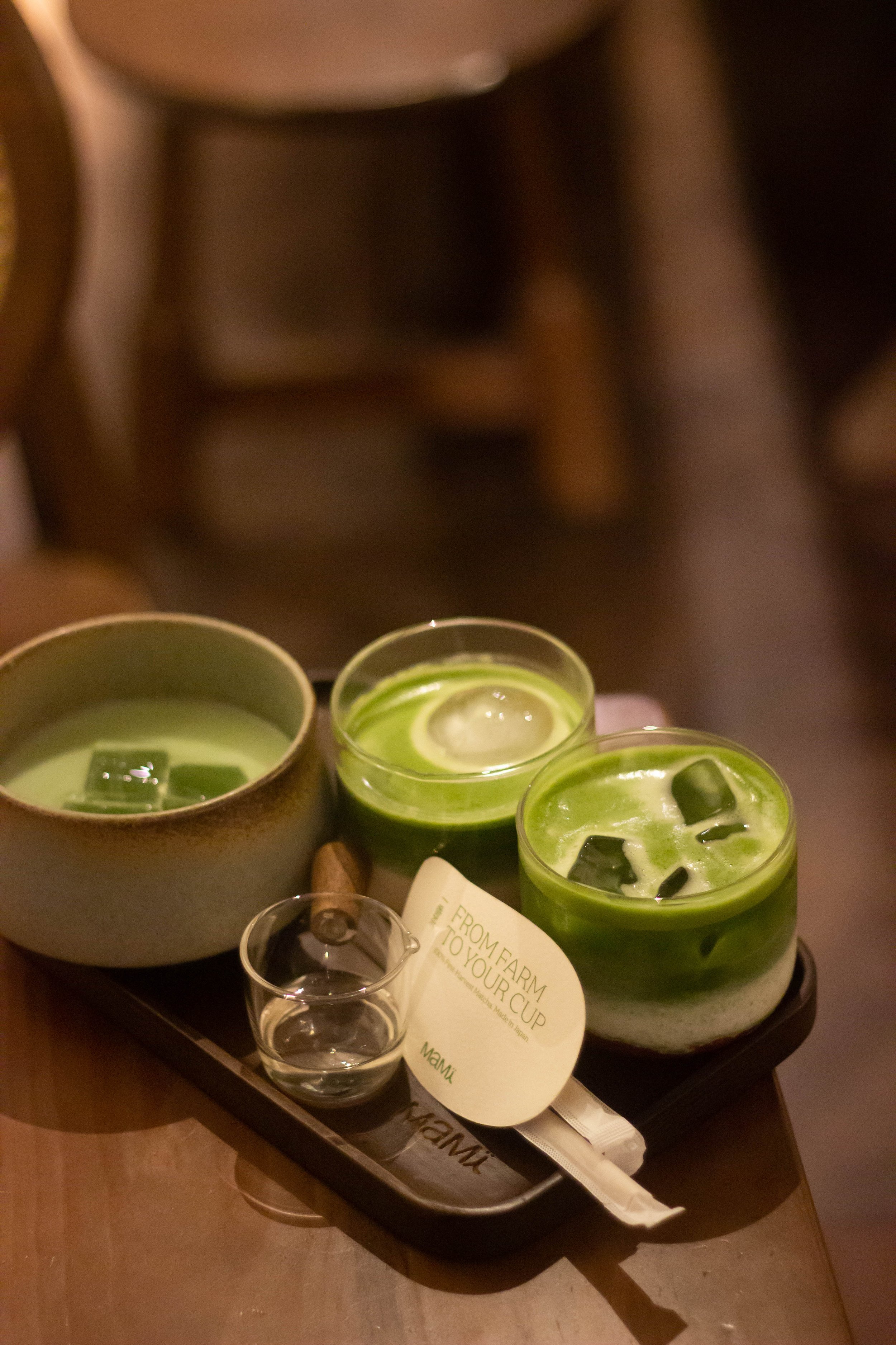 A tray with three cups of green tea with ice and lemon slices, and a small glass of water, on a dark tray at a restaurant table.