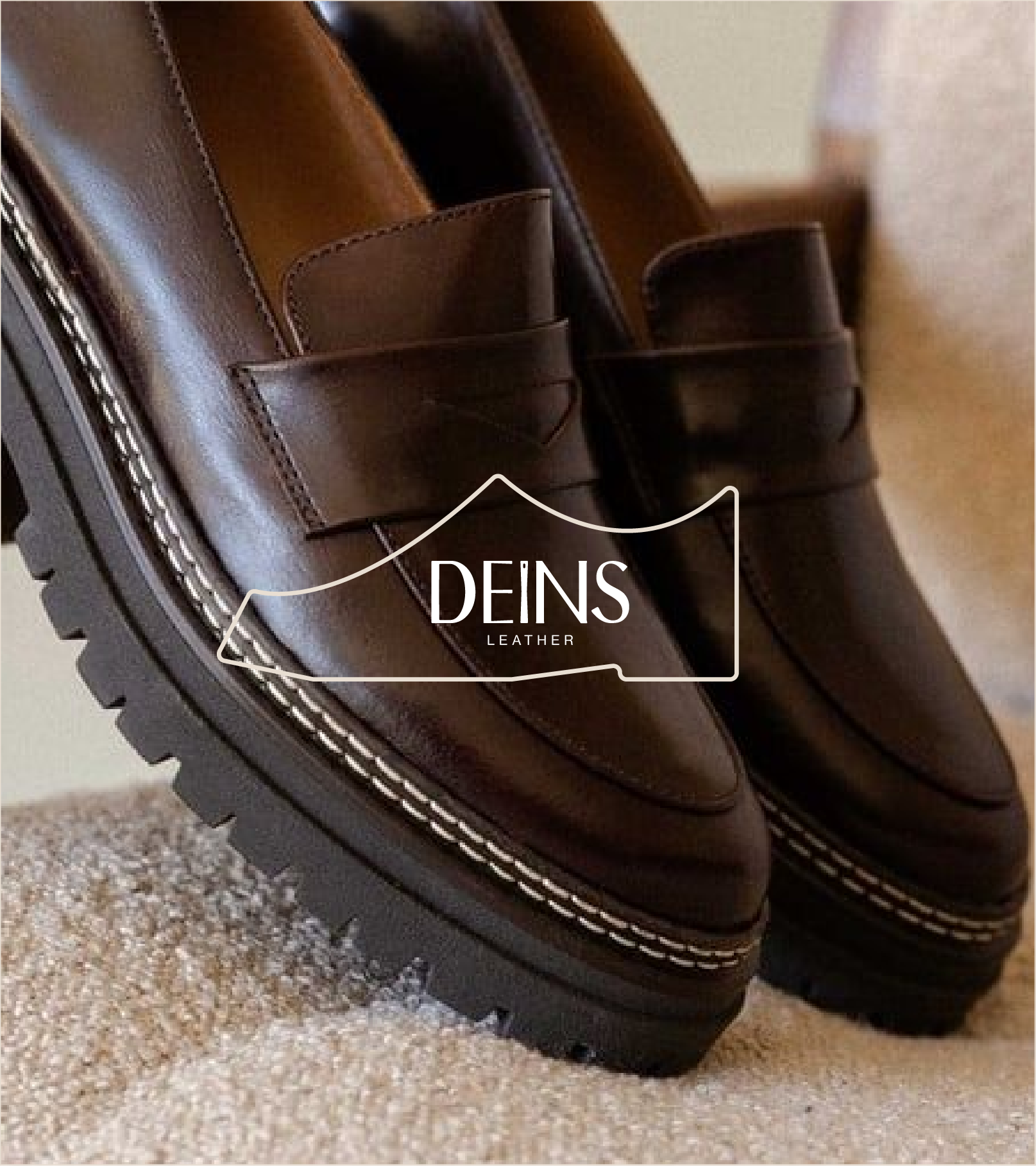 Close-up of brown leather dress shoes with chunky black soles on a beige carpet floor, featuring a strap with a stitched detail, branded with DEINS Leather logo.