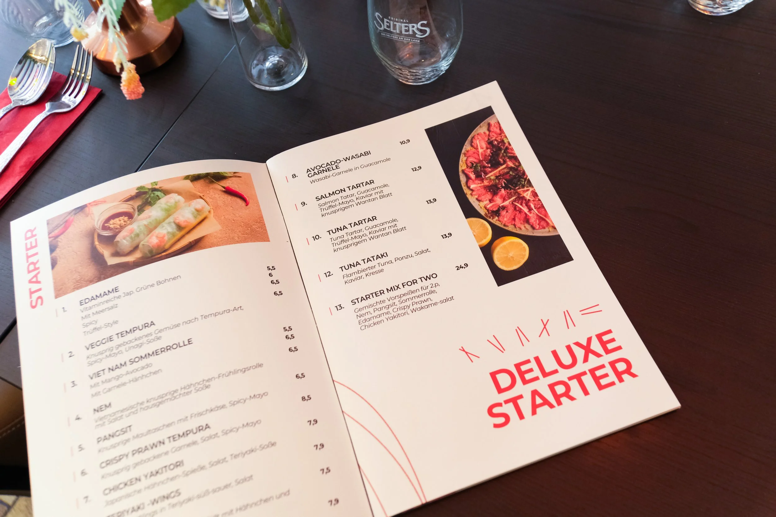 Open restaurant menu displaying starter options, including Edamame, Veggie Tempura, Viet Nam Sommerolle, and Chicken Yakitori, with a picture of spring rolls and a picture of sashimi with lemon slices on the cover page.