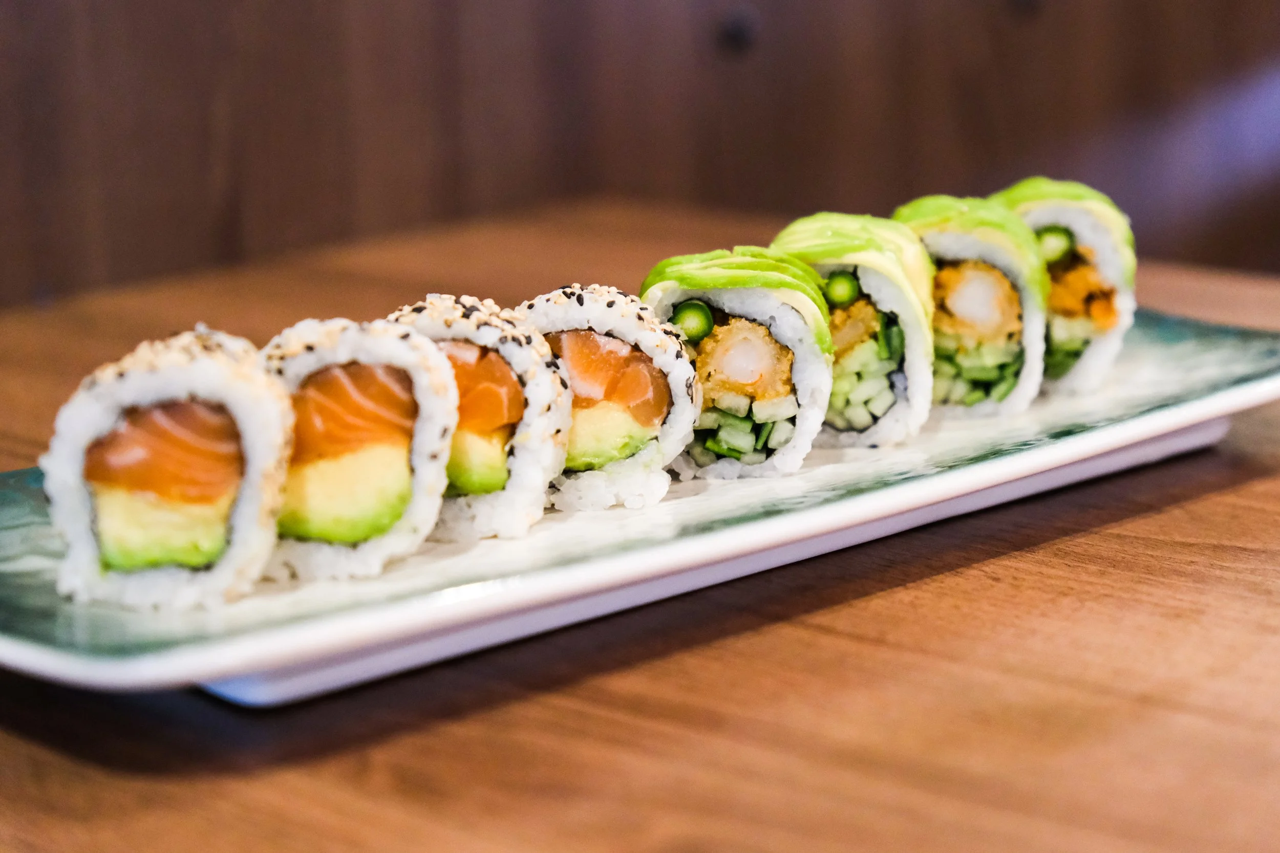 A rectangular ceramic plate with two types of sushi rolls on a wooden table.