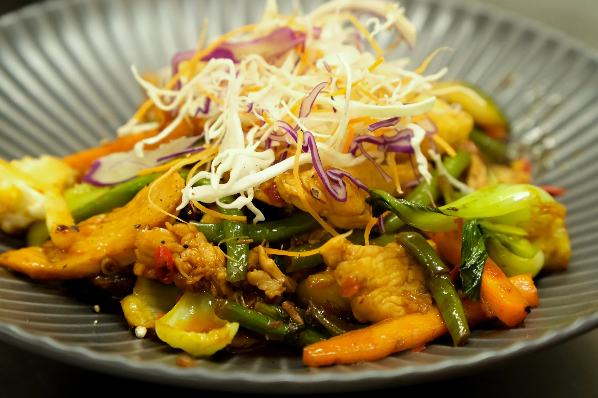 Stir-fried chicken and vegetables topped with shredded cabbage and carrots.
