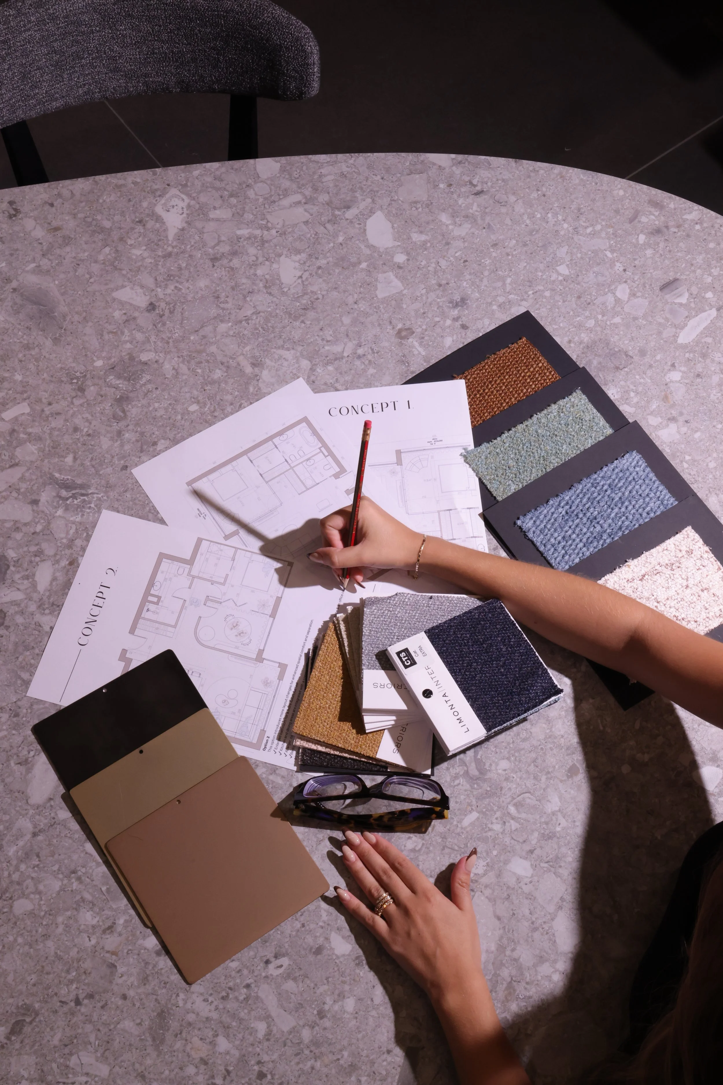 Interior design planning with fabric swatches, architectural blueprints, color samples, and a person’s hand holding a pencil over the designs. Formalivinh, Beirut Lebanon.