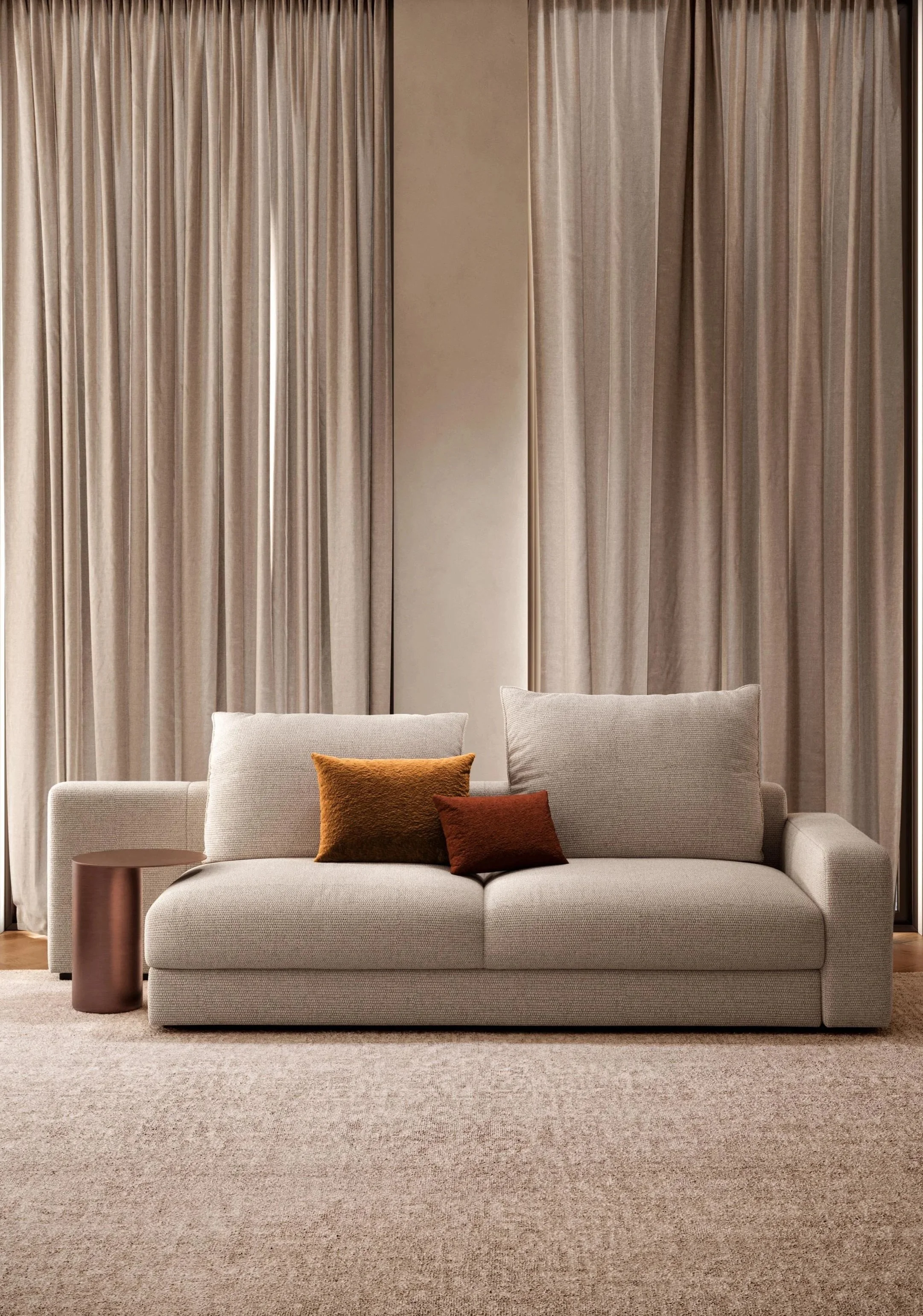 A modern beige sofa with three pillows in front of beige curtains in a stylish living room.