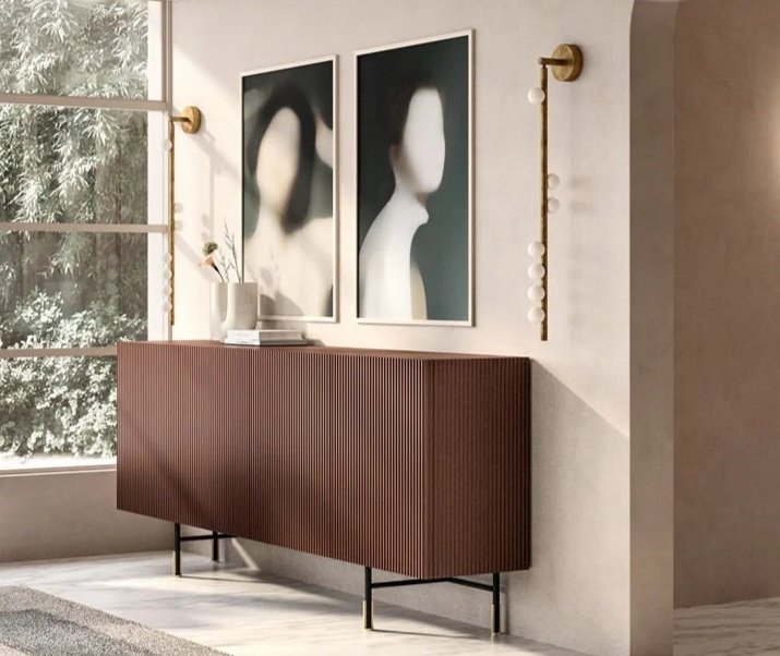 Interior of a modern room with a large window, a wooden sideboard, and three abstract art prints on the wall, with a decorative string of lights next to the artwork.