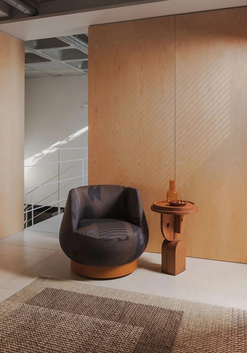 A modern interior corner with a patterned armchair and a small wooden side table holding a bottle and a bowl, set against a smooth wooden wall with a beige textured carpet on the floor.