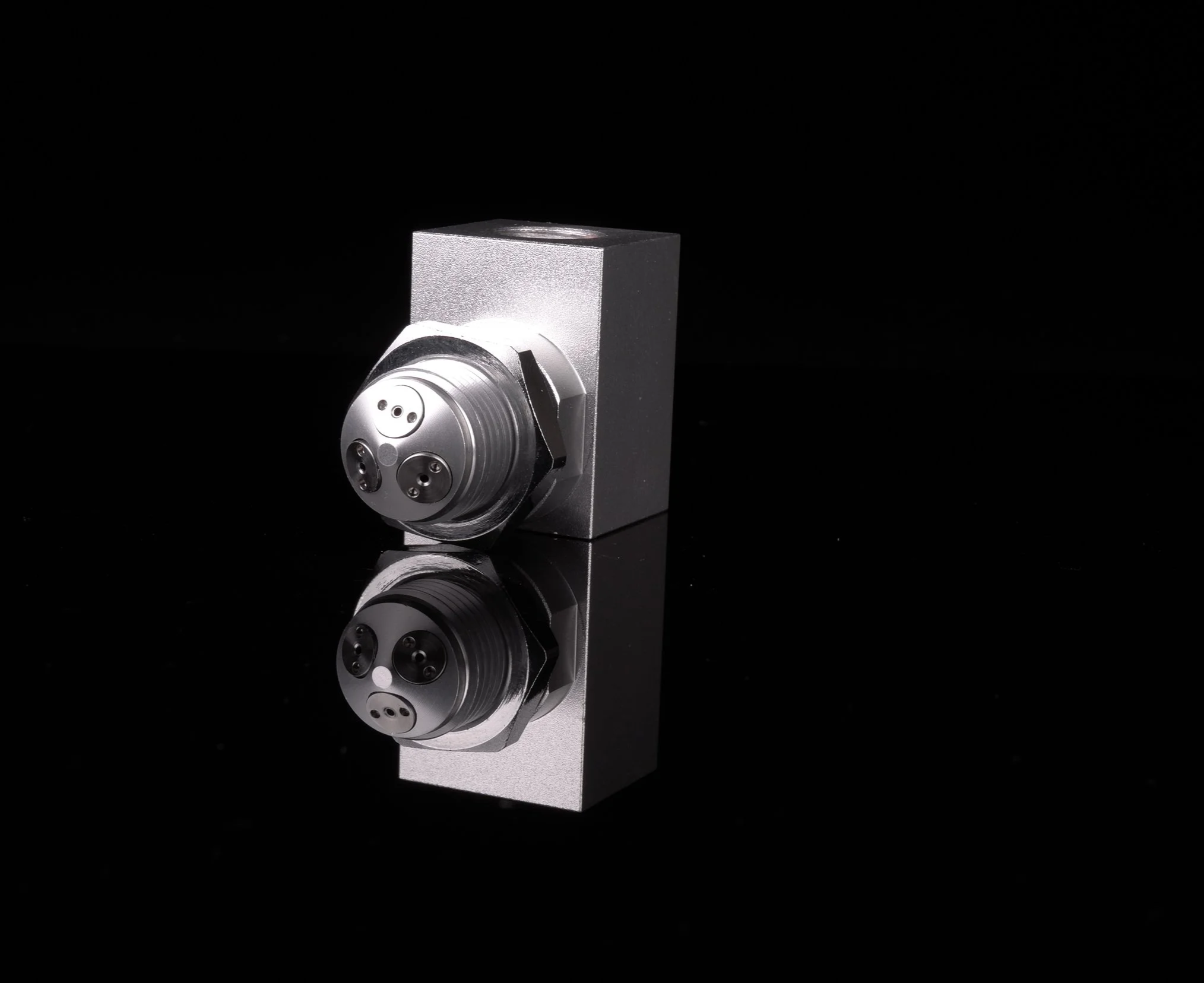Close-up of a precision part meant for liquid or gas industrial component with a cylindrical feature, mounted on a black background with reflection.